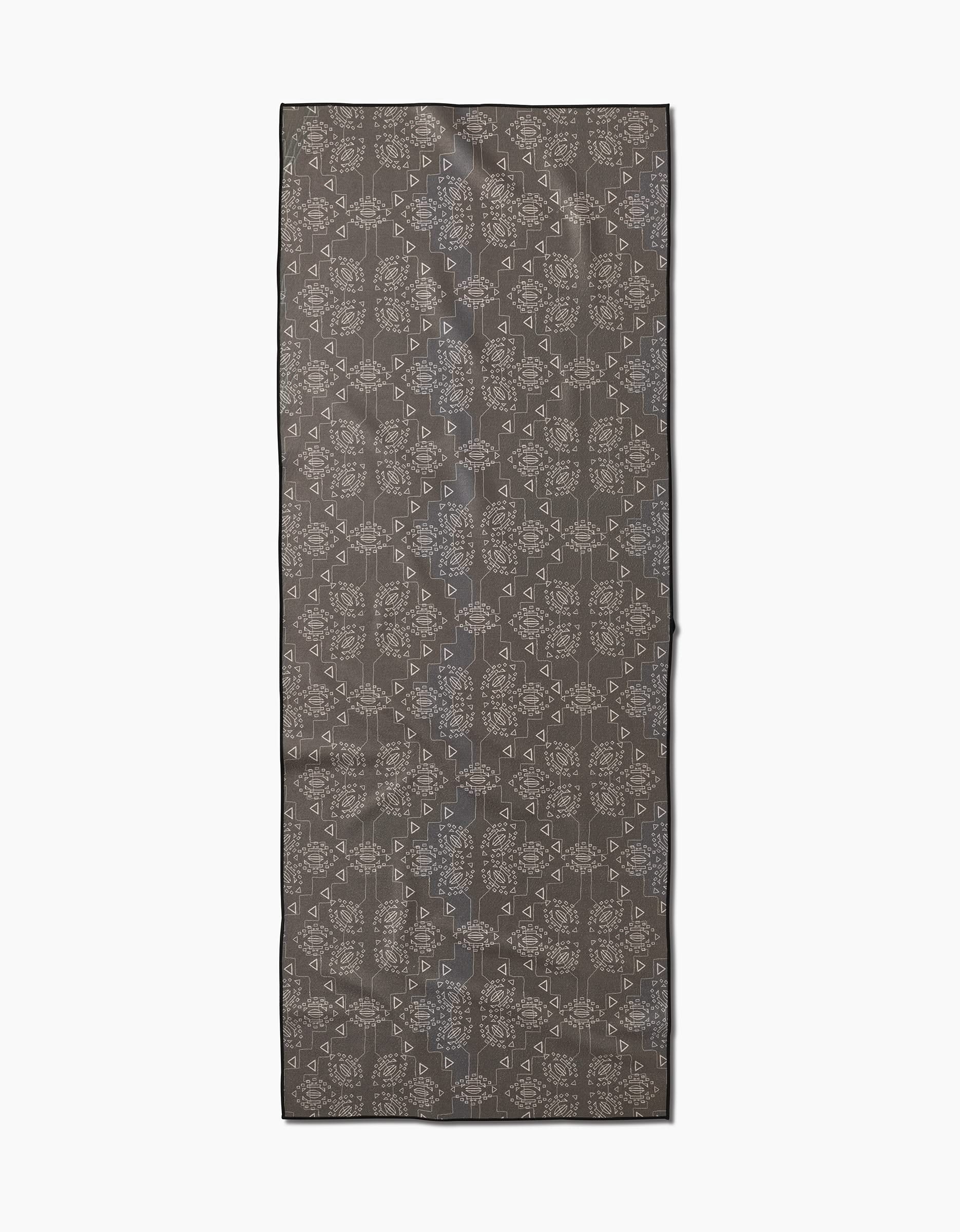 The Ash Cascade Mountain Bloom scarf features a dark gray background with an intricate light gray geometric pattern, reminiscent of a recycled yoga towel, and is shown laid flat on a white surface.