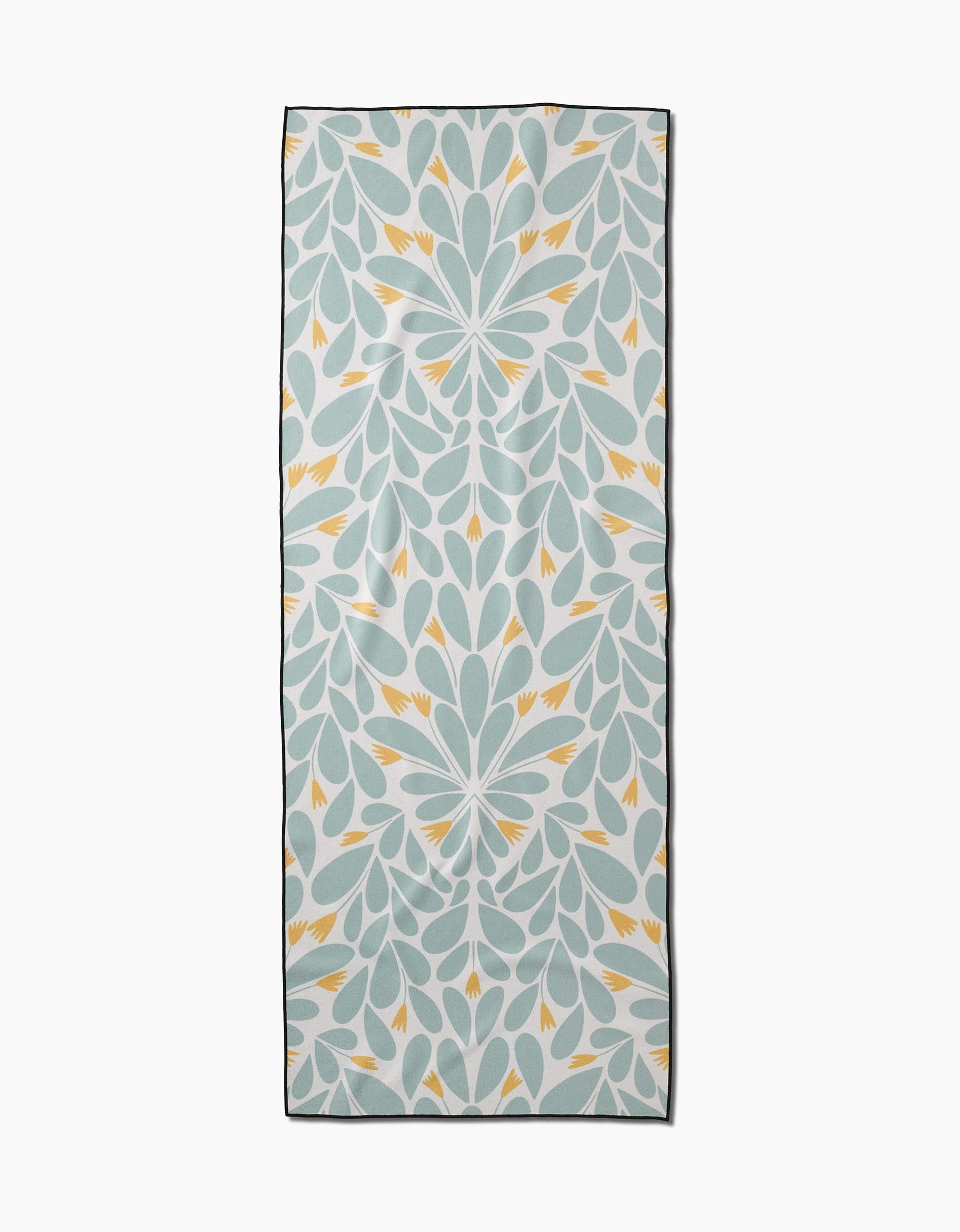 The Mustard Pinwheel yoga towel by Rebecca Woolbright features a symmetrical leafy motif with light blue, white, and yellow accents bordered by a thin dark edge. Made from recycled materials, it brings charm to your mindful practice.