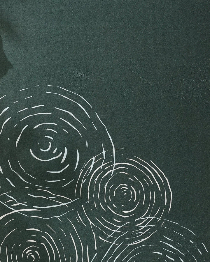 The GEOMETRY Om yoga towel has a dark green non-slip surface with white, irregular concentric circles resembling tree rings clustered on the lower left and center.