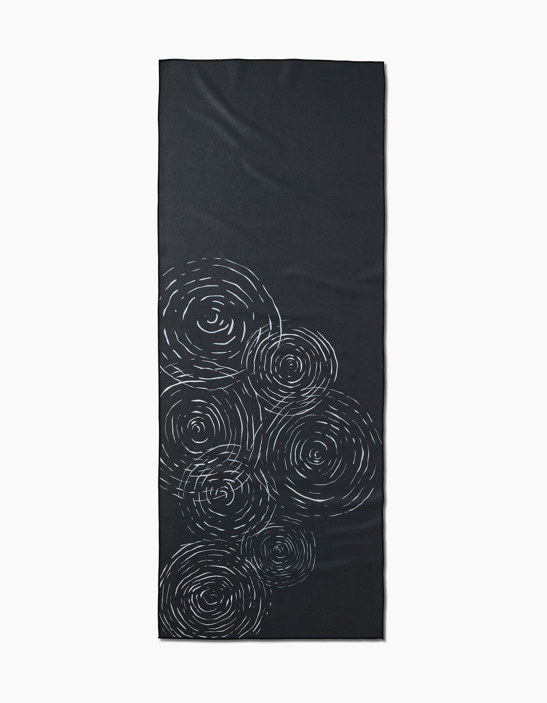 The GEOMETRY Om is a rectangular black yoga mat made from recycled materials, featuring white swirling circular patterns clustered on one end.