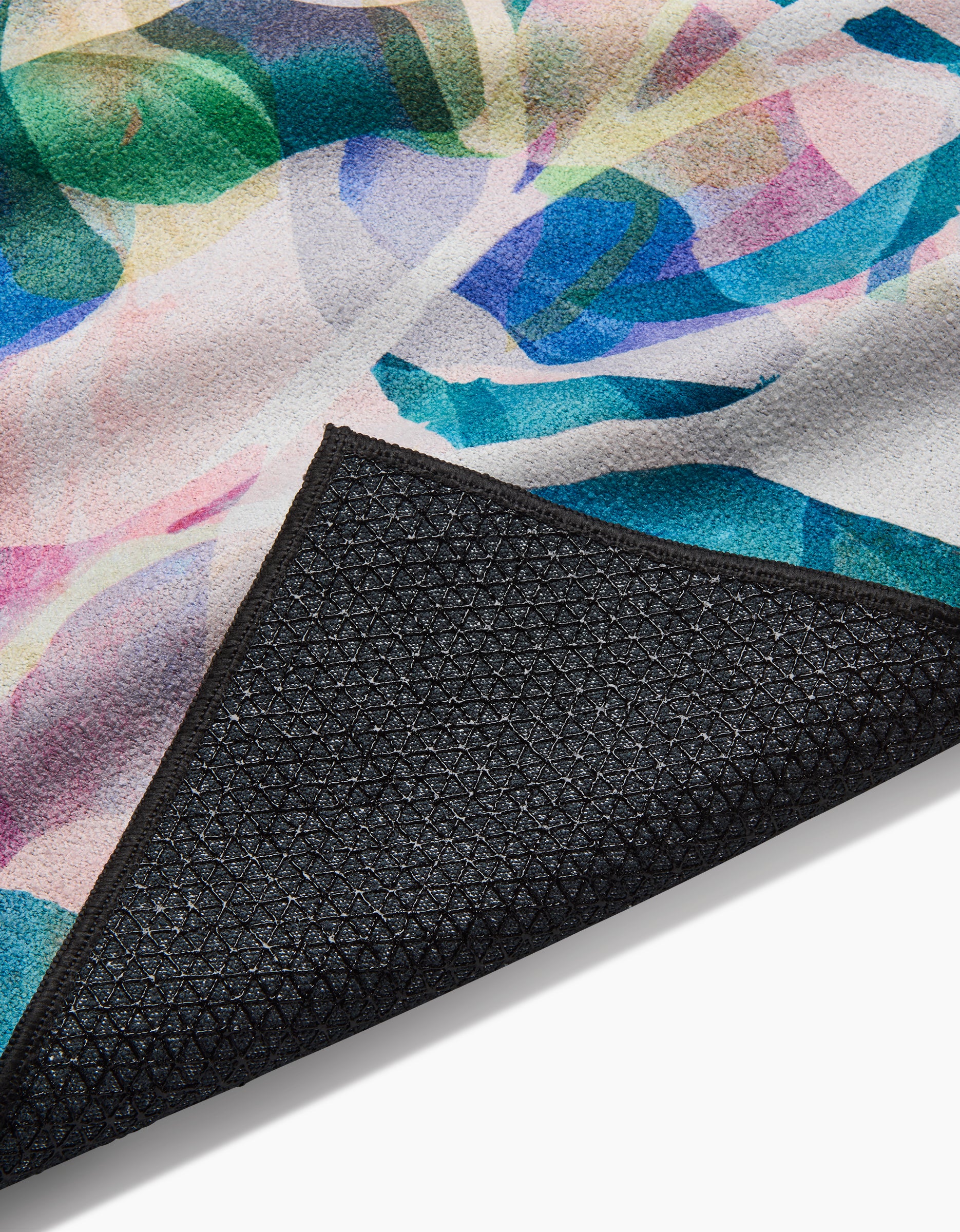 A close-up of the Rachel Parker Painted Foliage yoga towel shows its vibrant abstract pattern, with one corner flipped to reveal a textured black silicone grip non-slip backing.