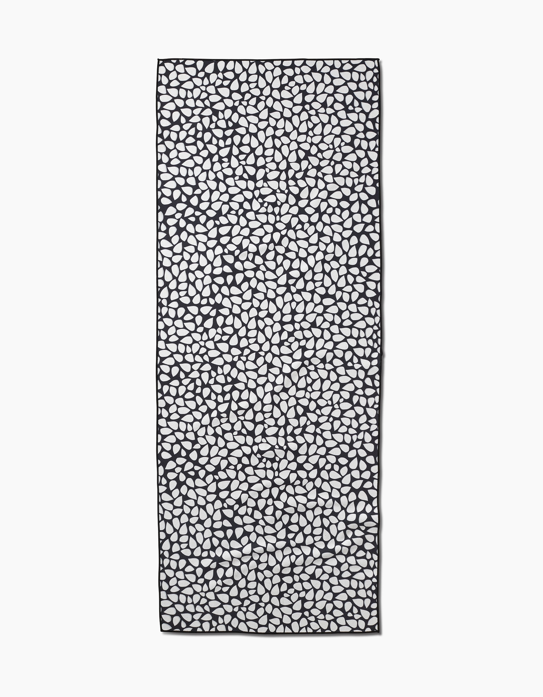 The Pebbles scarf by Marina Solodka features an all-over black pebble pattern on a white background, inspired by recycled yoga towels. The rectangular scarf is shown laid flat.