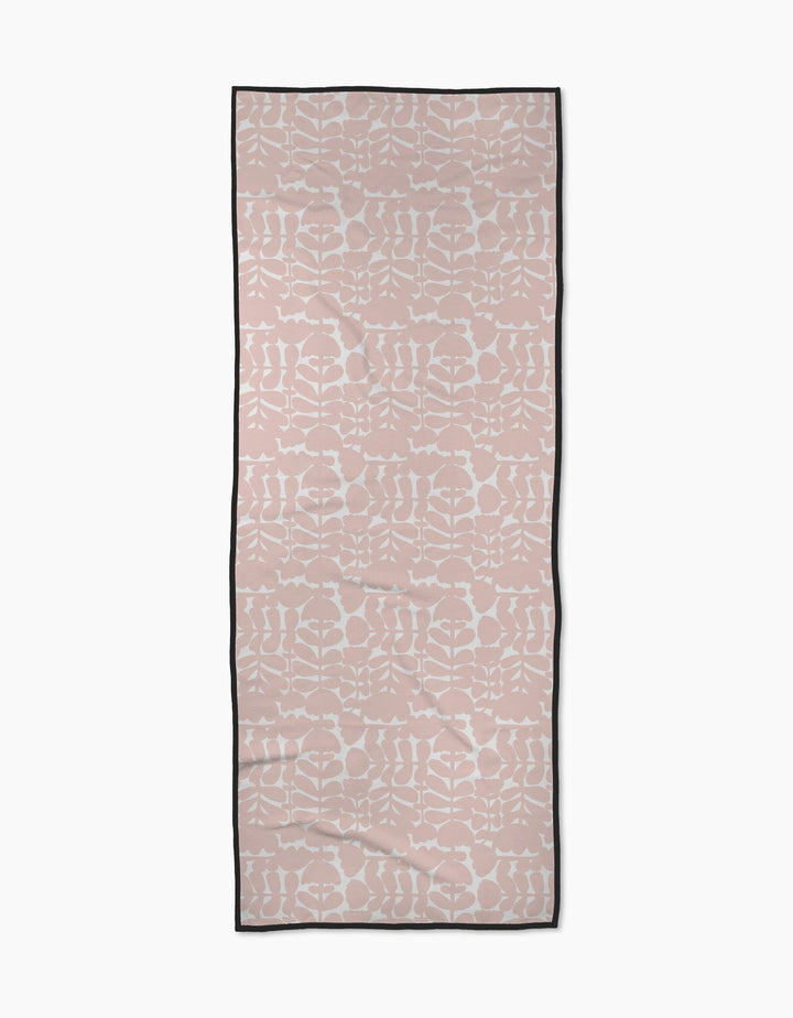 The Pink Scandi Flowers yoga towel by Katie OShea is rectangular, light pink with a white symmetrical floral pattern and a thin black border, shown flat on a white background.