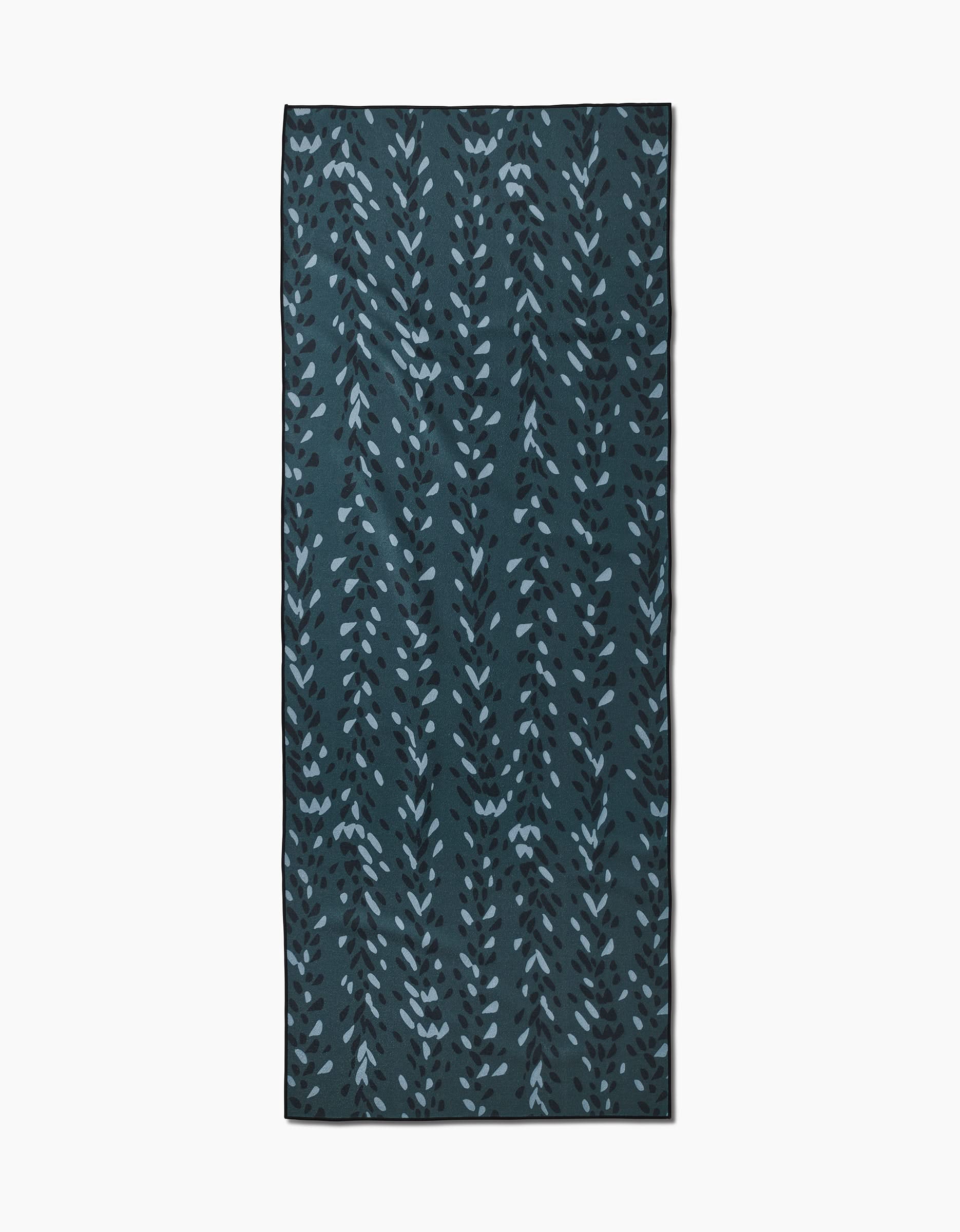 The Pose yoga towel by GEOMETRY features vertical leafy blue branches on a dark teal background and is crafted from recycled materials.