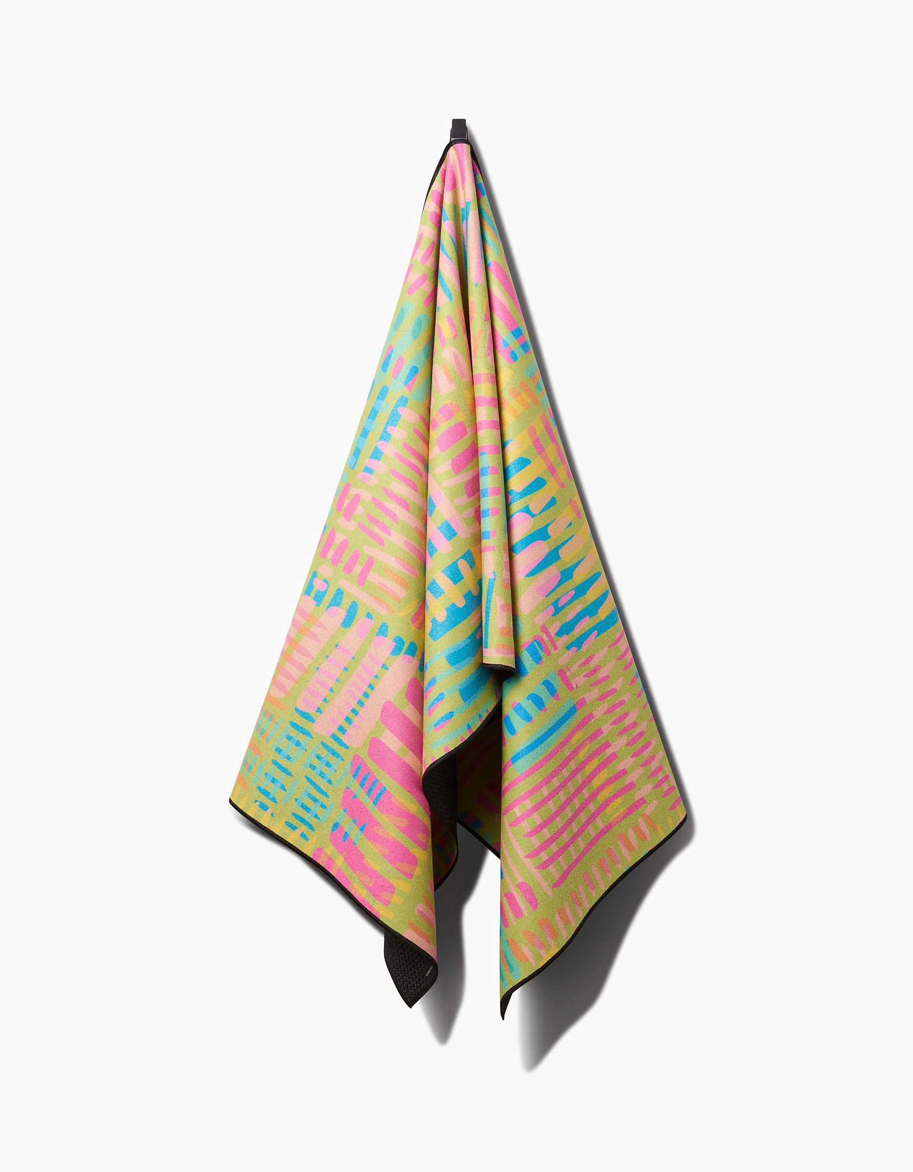 The Sareka Unique Positive Vibes yoga towel, made from recycled materials, features a vibrant geometric pattern in pink, yellow, blue, and green and is displayed hanging against a plain white background.