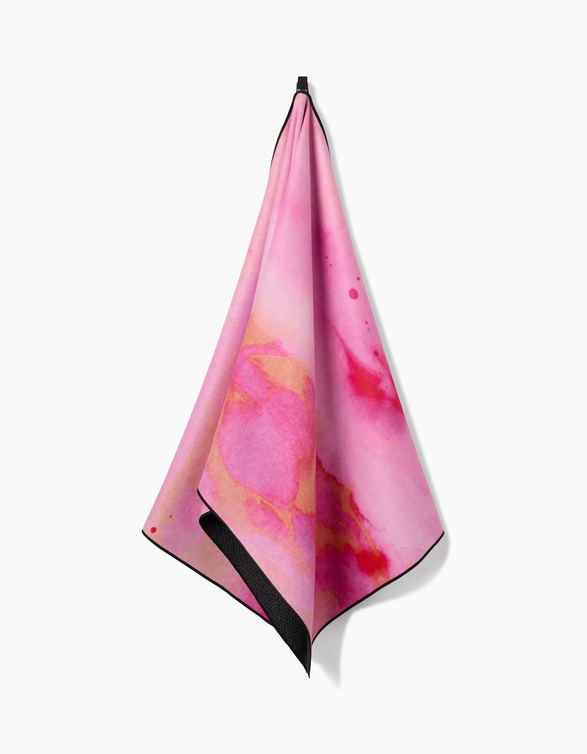 The Purity yoga towel by Geometry, made from recycled materials, features abstract watercolor patterns in pink, peach, and red hues and is shown hanging against a plain white background.
