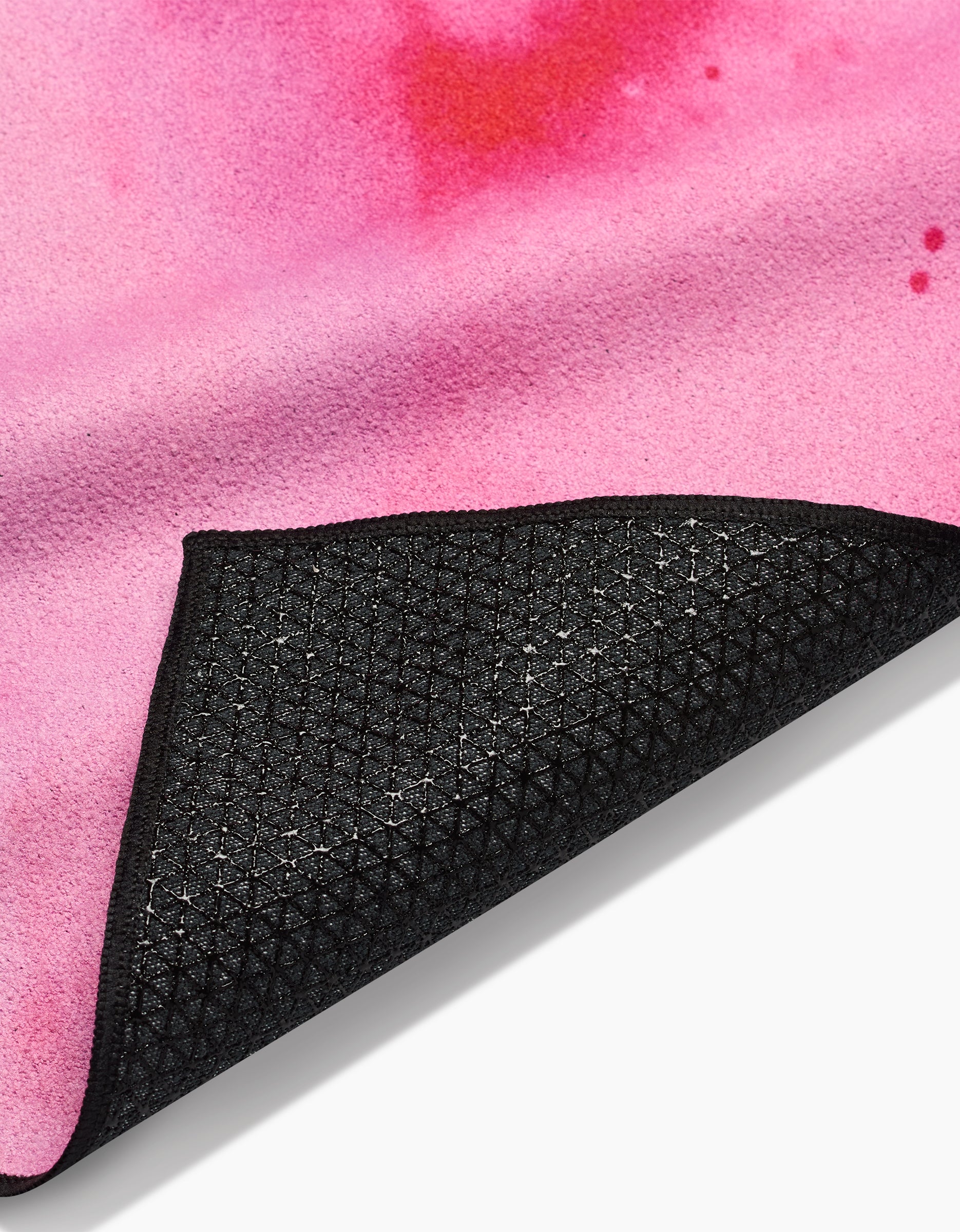 Close-up of Geometry’s Purity yoga mat with a pink, watercolor-like top and textured, non-slip black silicone grip underside, partially folded to display both surfaces.