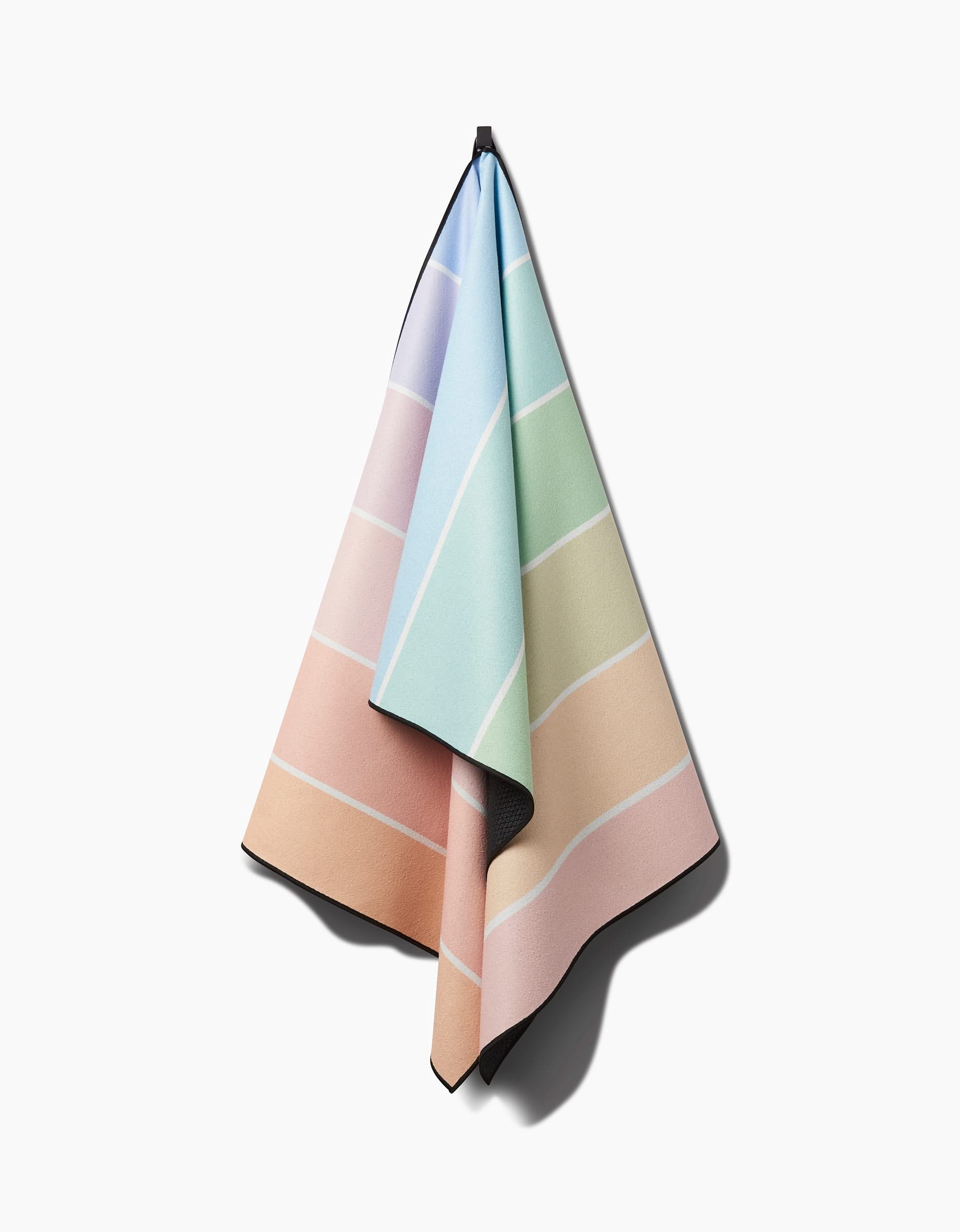 The GEOMETRY Rainbow Pastel is a soft, slip-resistant yoga towel featuring pastel blue, green, pink, and peach color blocks separated by thin white lines and displayed on a white wall.