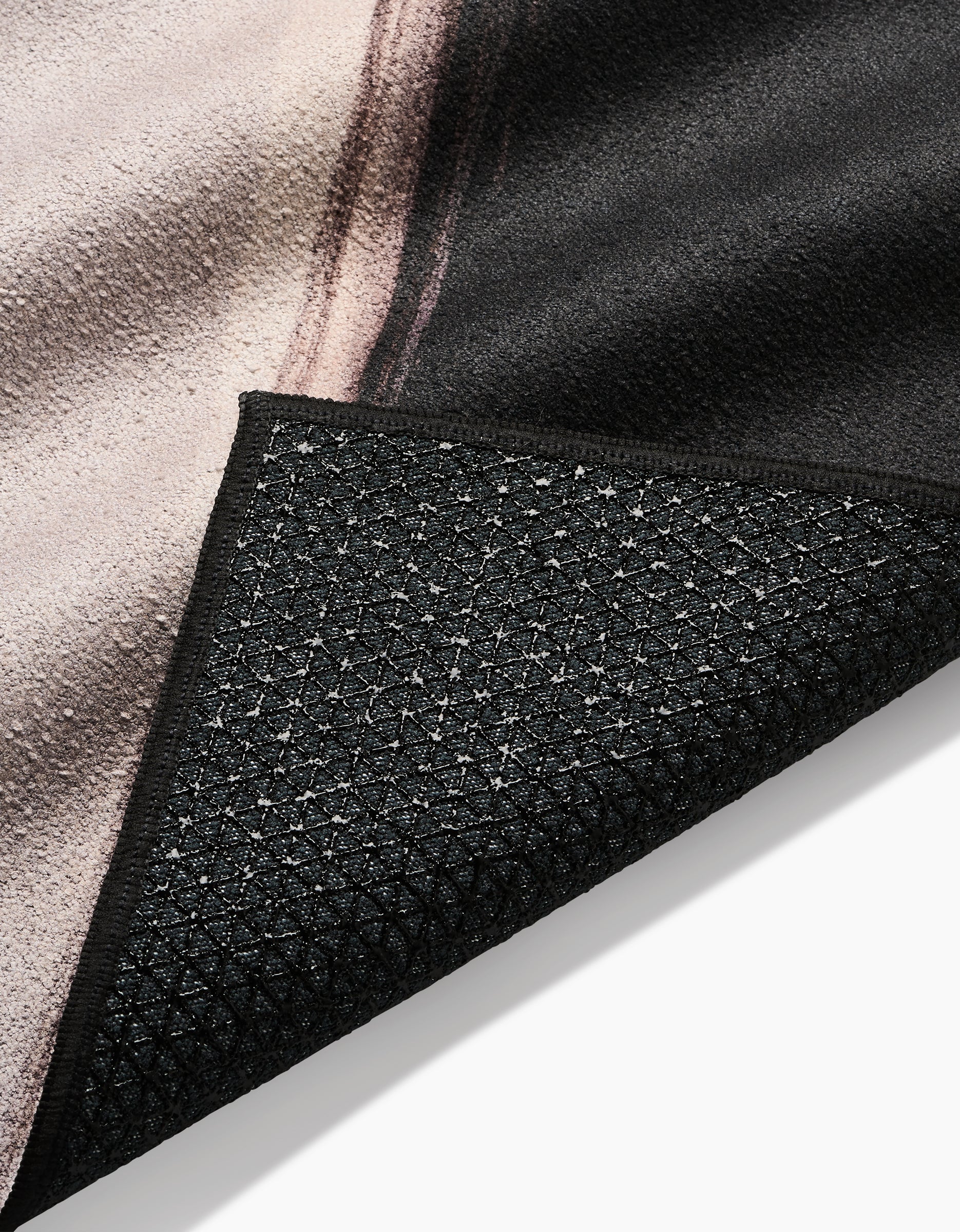 A close-up of Rhythm by Jennifer Janesko shows the textured, slip-resistant yoga towel-style black backing and part of the patterned front in black, beige, and brown.