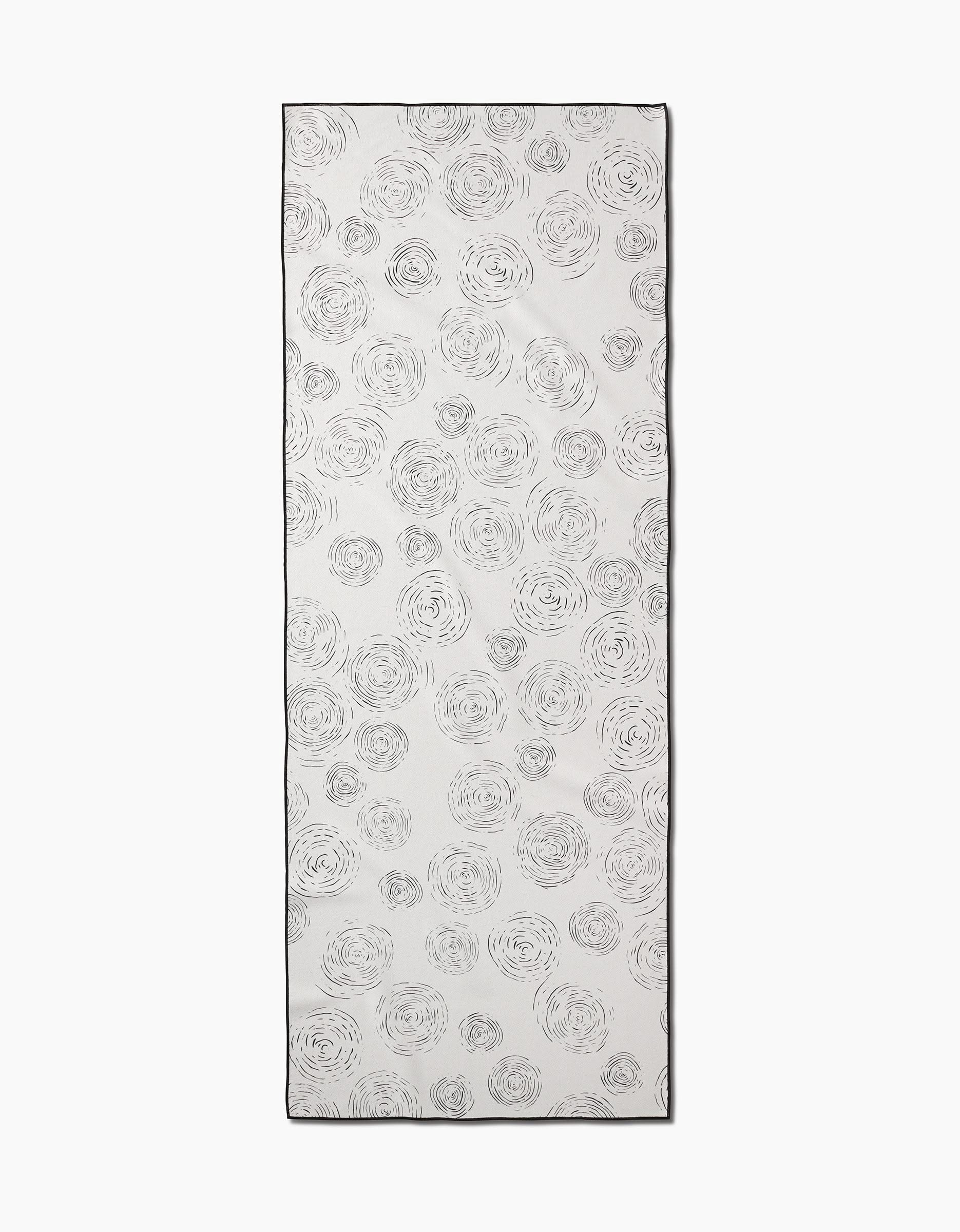 The Rhythmic yoga towel by GEOMETRY is a rectangular white towel with light gray, hand-drawn spiral circles scattered across the surface and finished with a thin black border.