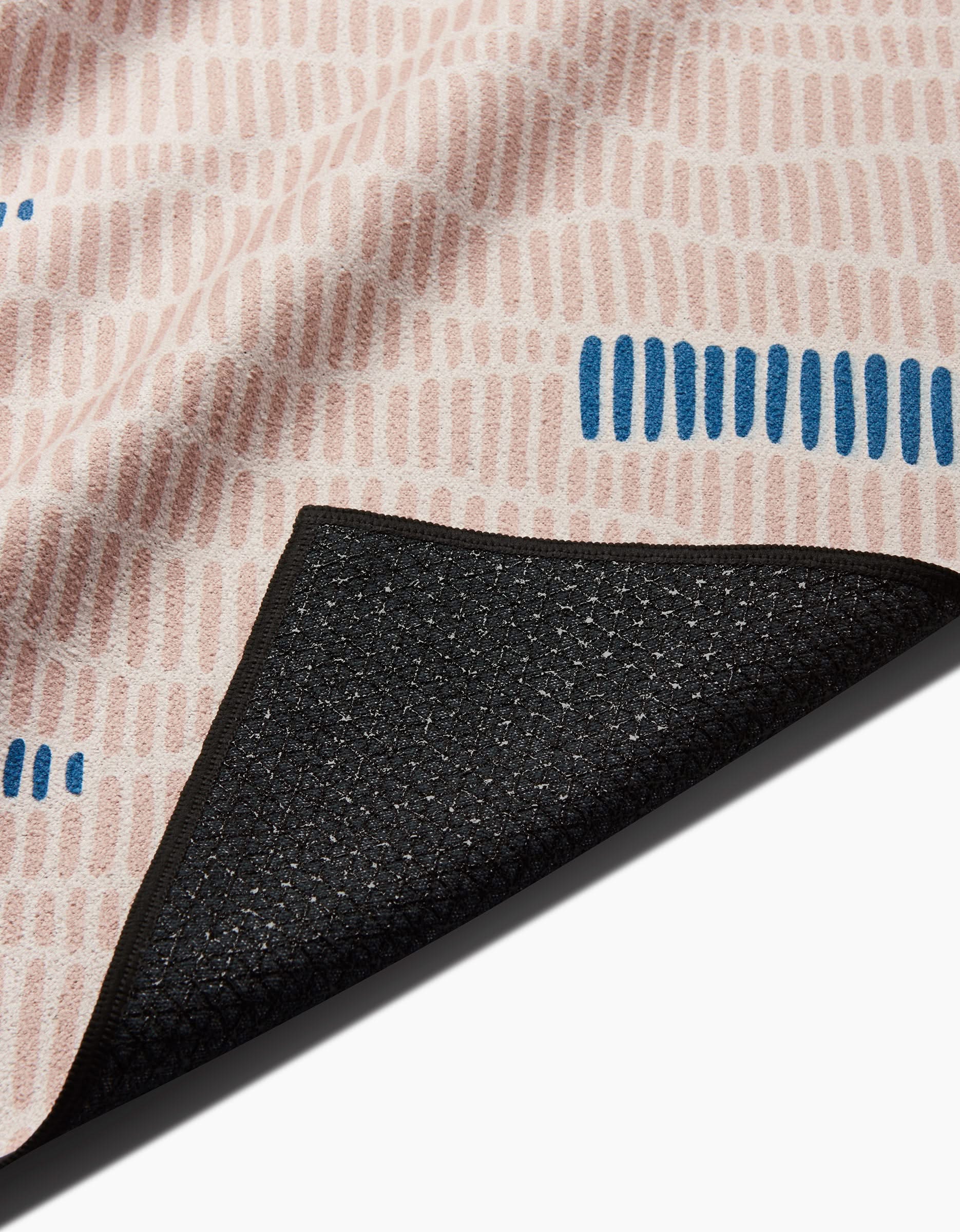 A close-up of the Ridgeline yoga towel by Twig + Spark, featuring pink and blue dashed patterns on textured slip-resistant fabric with a black non-slip backing, shown partially folded.