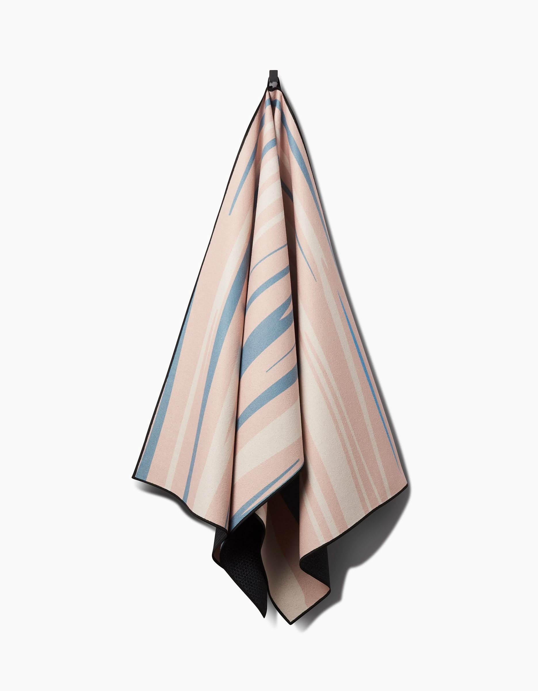 The GEOMETRY Root recycled yoga towel, featuring a soft pink, beige, and blue abstract striped pattern with black trim, hangs from a black hook against a white background. Its slip-resistant for optimal performance.
