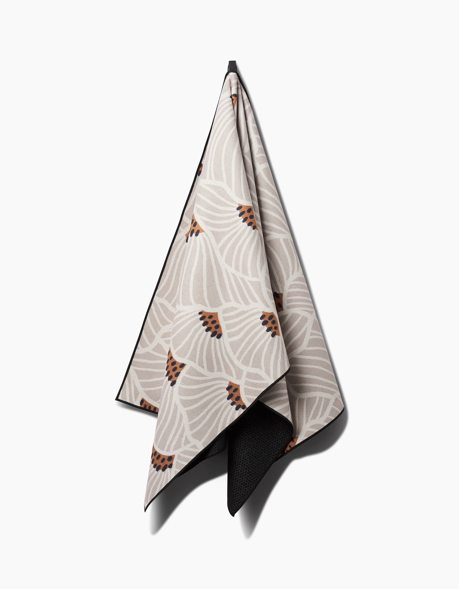 The Amy MacCready San Diego yoga towel, featuring a beige base with a white and brown abstract floral design, made from recycled materials, hangs neatly against a plain white background.