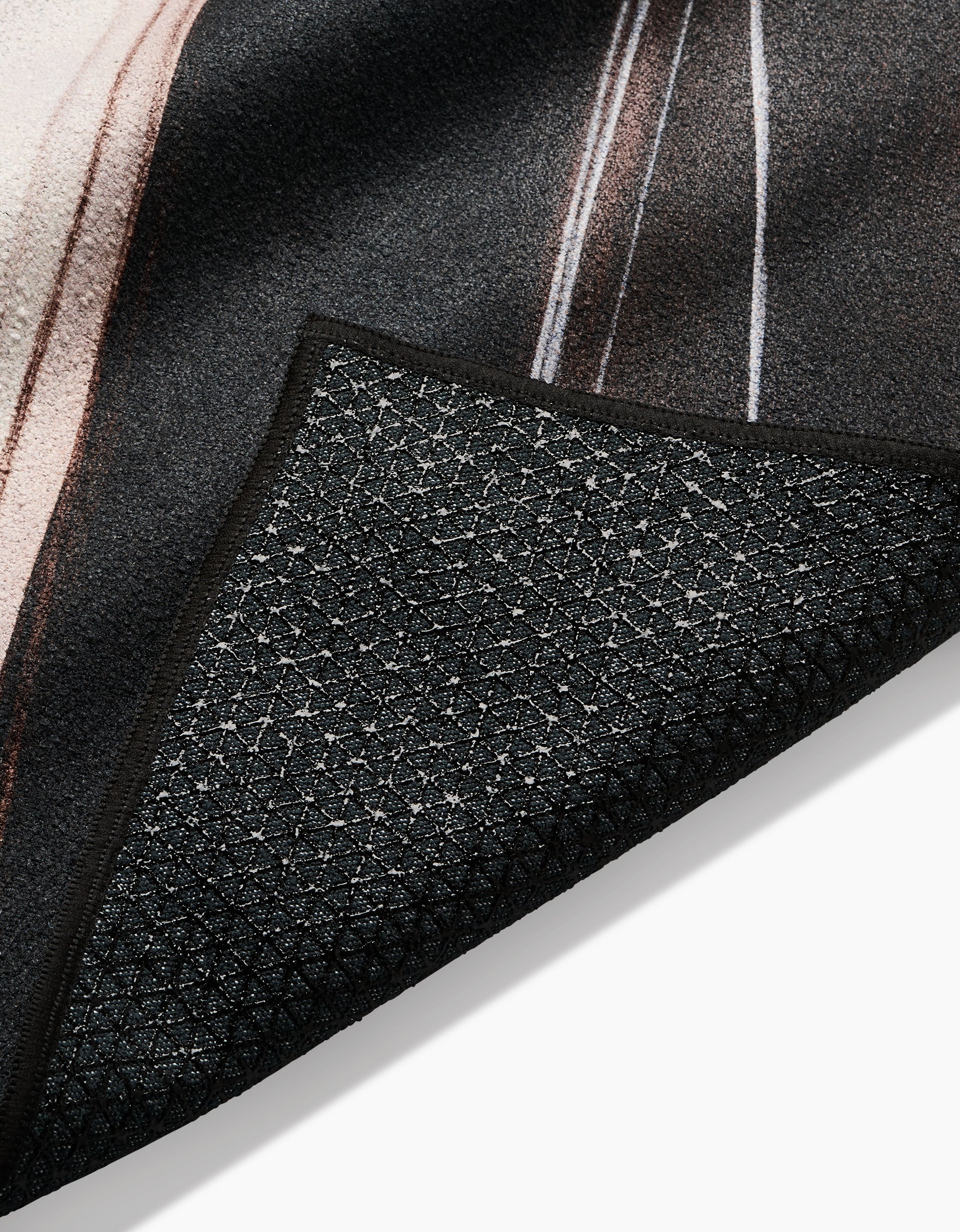 A close-up of a corner of the Seduction yoga towel by Jennifer Janesko, highlighting its black textured non-slip surface, detailed backing underneath, and a glimpse of the patterned top.
