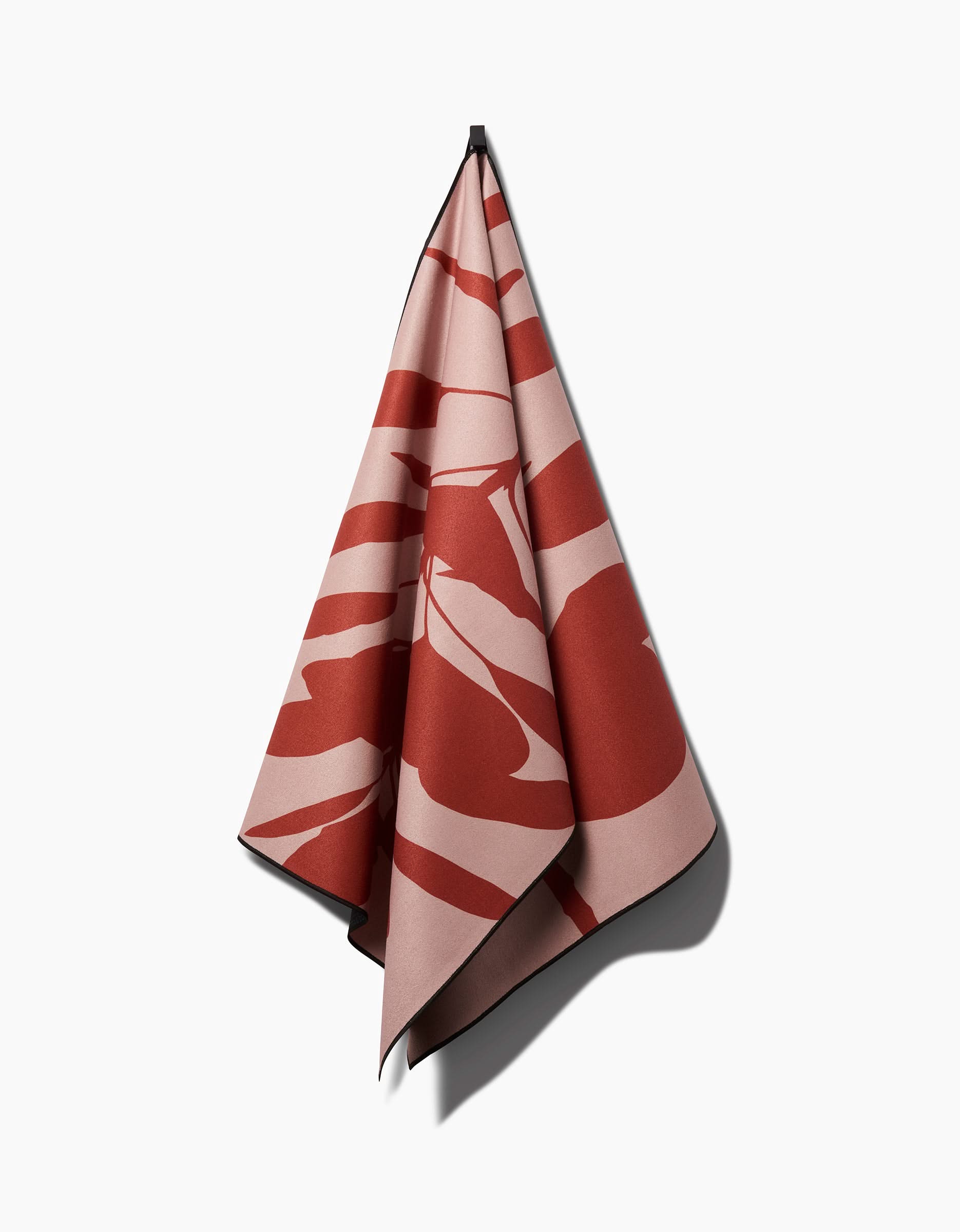 The Smoketree yoga towel by PrintedPlant features a bold, abstract red and pink pattern and hangs neatly from a single point against a white background. Made from recycled materials, it blends standout style with sustainability.