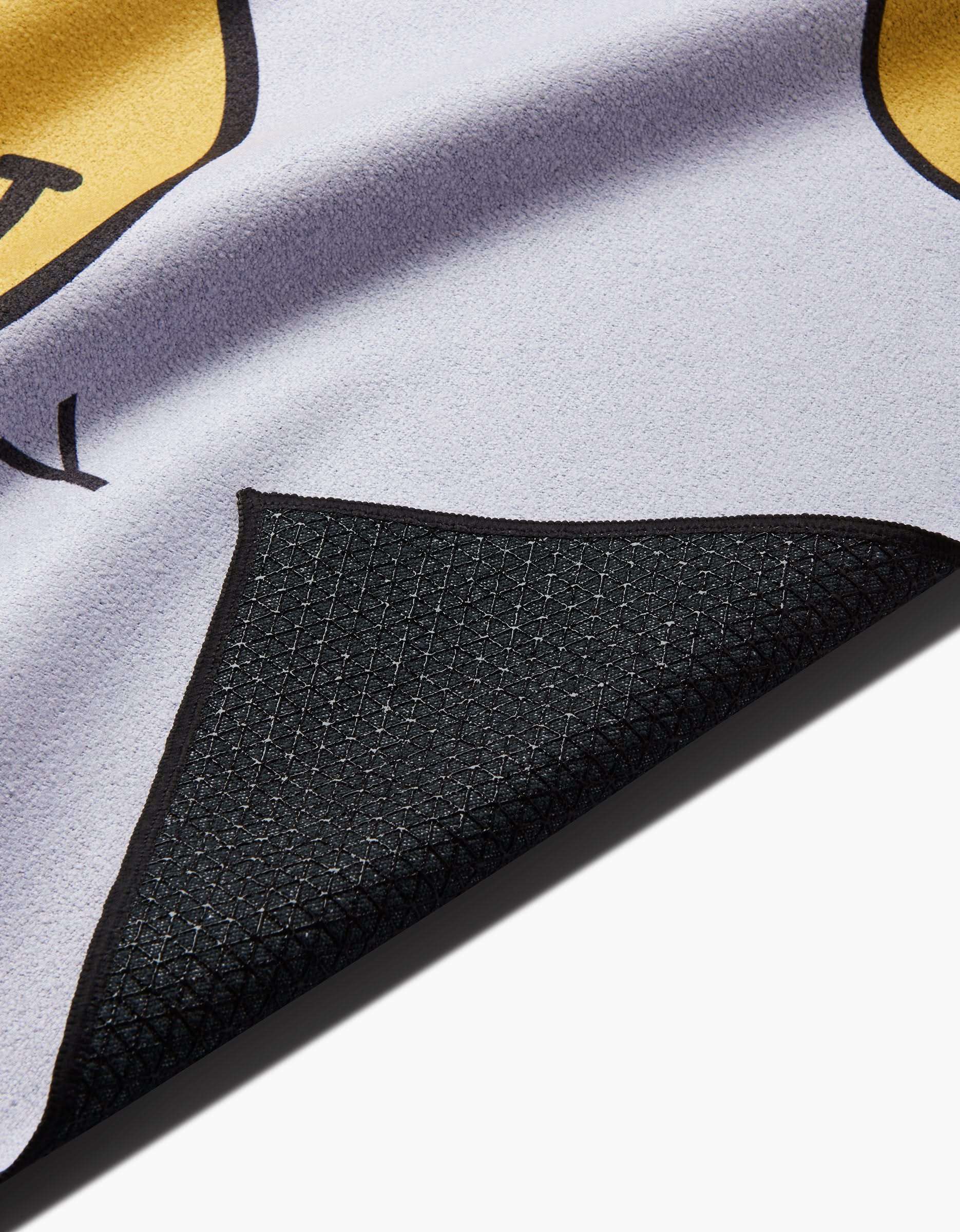 Close-up of the Soul Happy yoga towel by Quotes by Christie, featuring a black slip-resistant underside and a yellow and purple design. The curled edge displays both surfaces, each crafted from recycled materials.