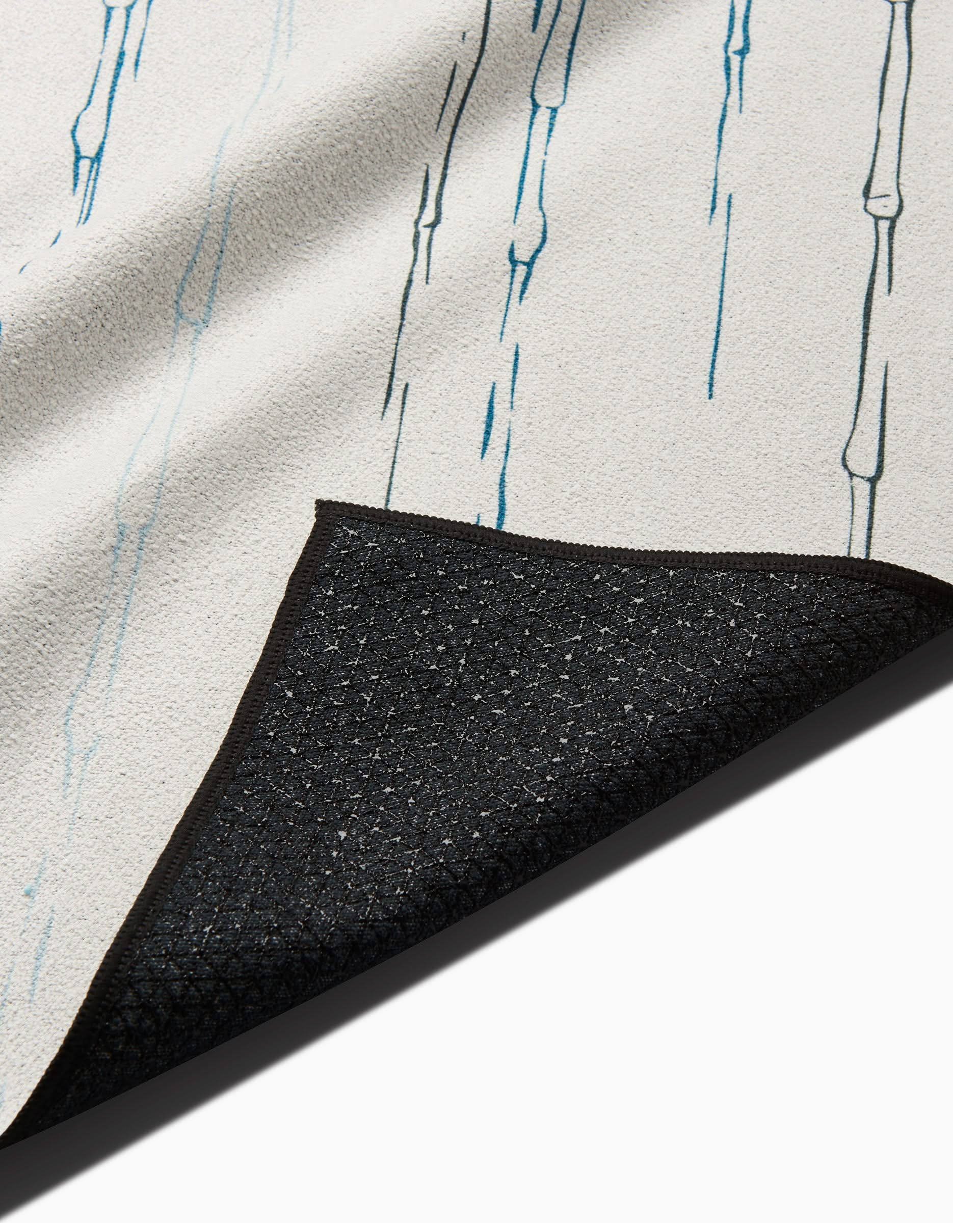 A close-up of the GEOMETRY Stilts rug shows its textured black non-slip backing and a white surface with light blue vertical streaks, making it perfect for use as a non-slip yoga towel during workouts.