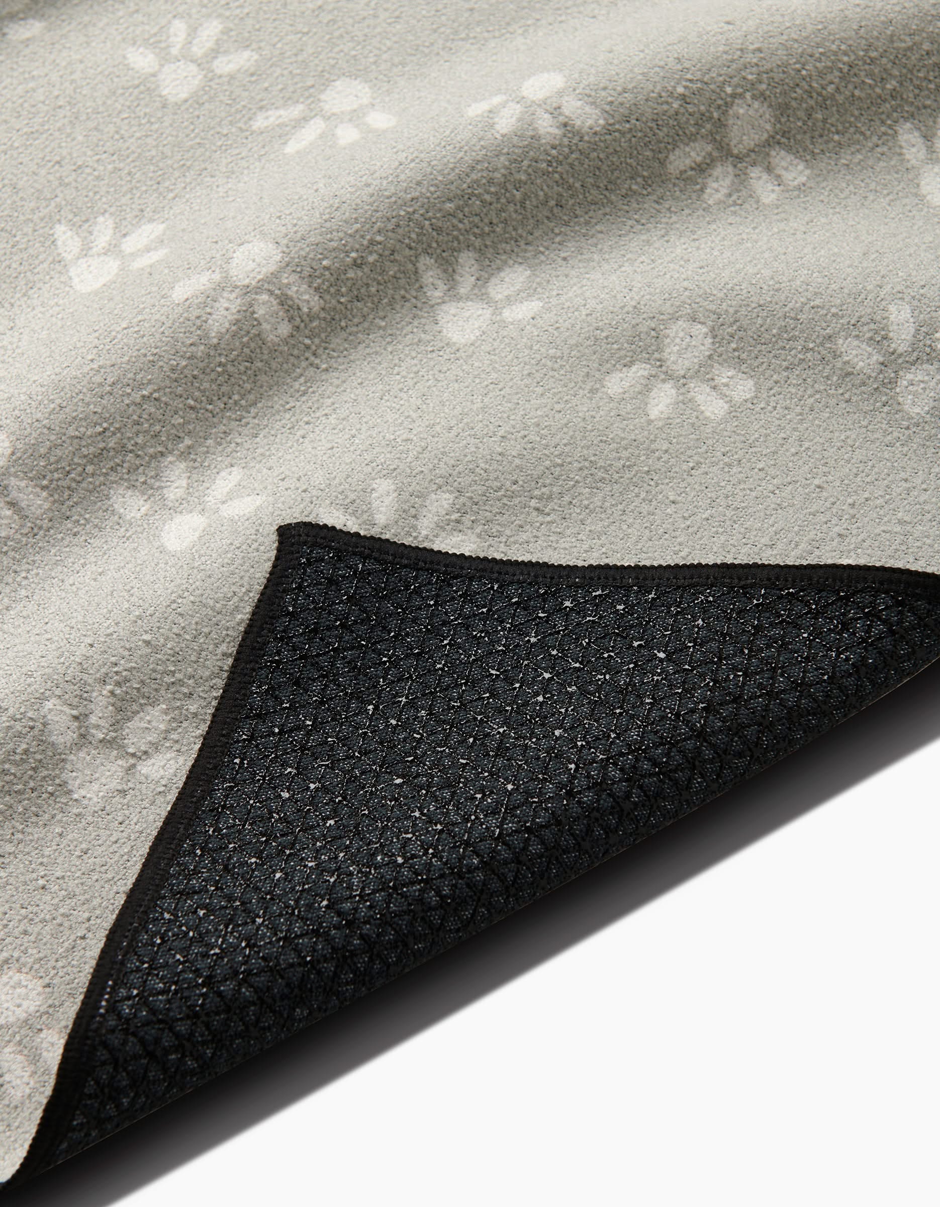 The Anee Shah Sun Bursts blanket is shown in light gray with white paw prints, partially folded to display its textured black non-slip yoga towel backing.