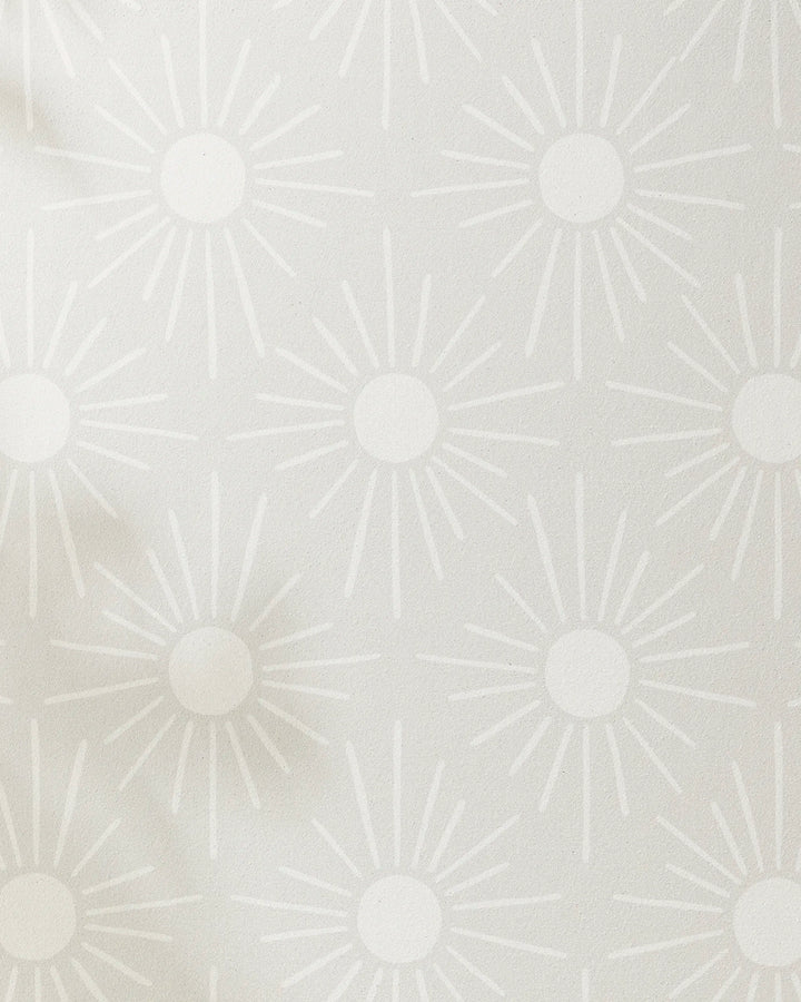 Sunny Geo wallpaper by Hufton Studio features a light grey background with white sunburst shapes—each with a central circle and radiating lines—for a modern, calming effect reminiscent of yoga towel designs.