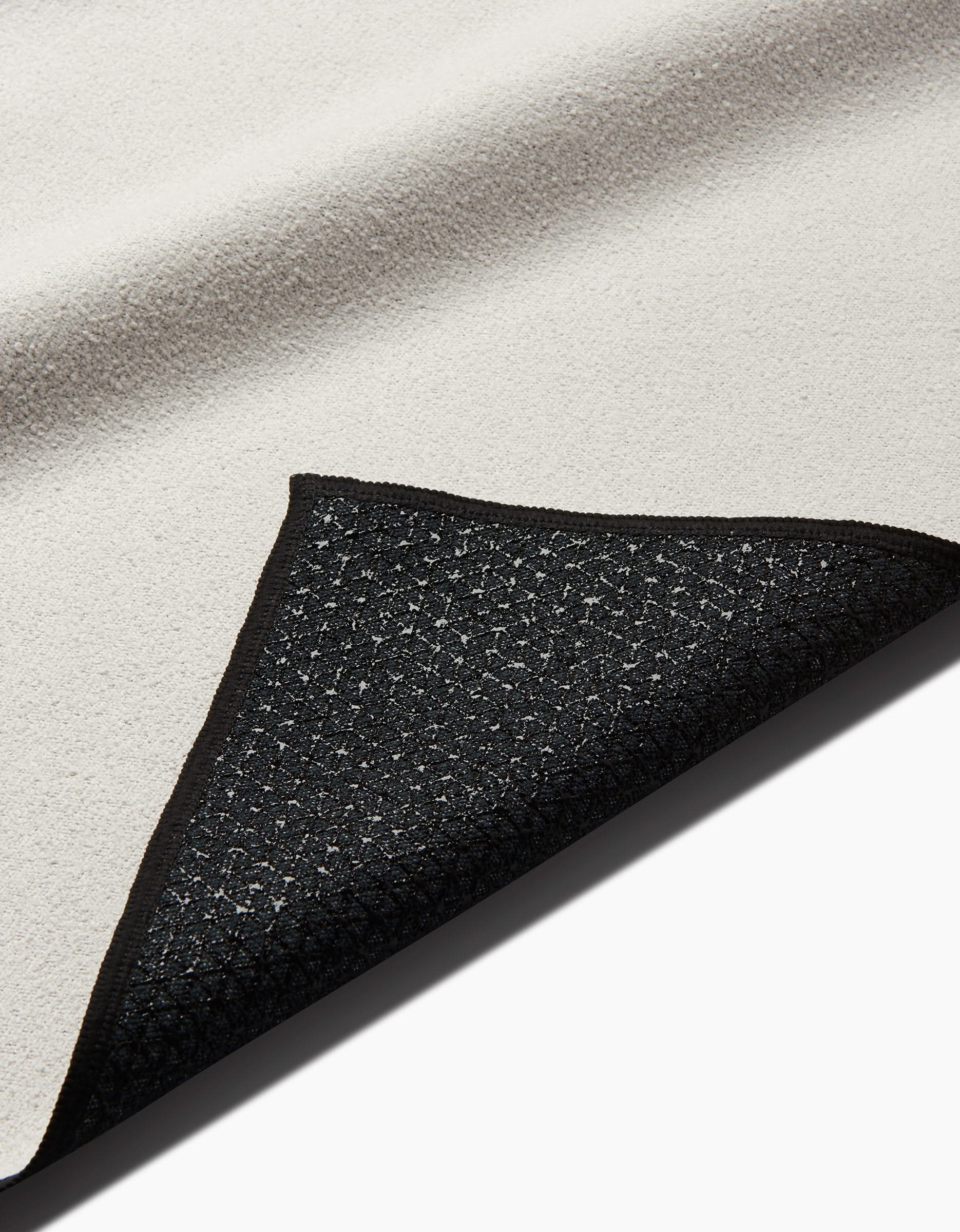 A close-up of the Take It Slow rug by Graphics and Grain shows one corner flipped to reveal its black, patterned, slip-resistant yoga towel backing.