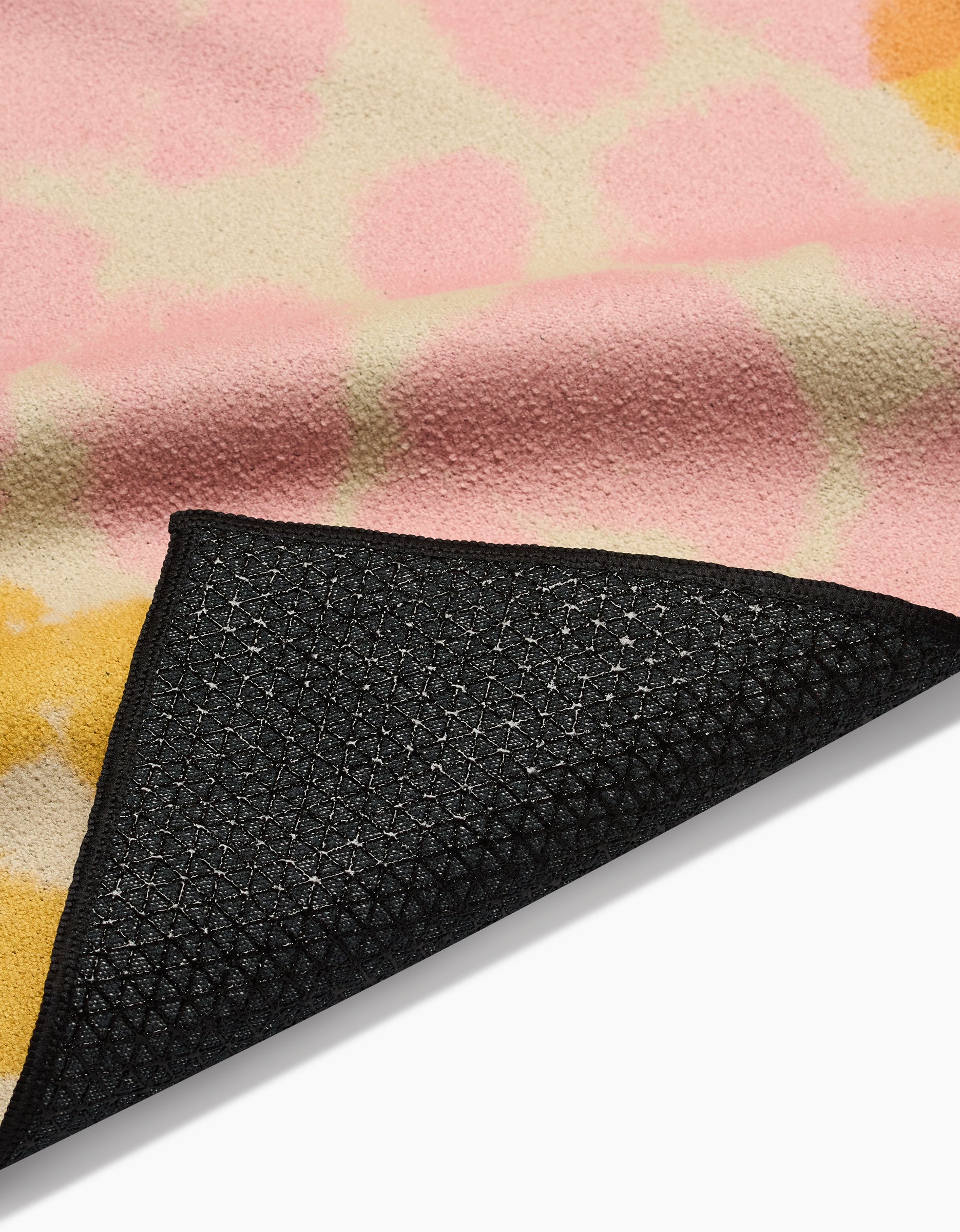 A close-up of the GEOMETRY Whimsy yoga towel, displaying its pink, yellow, and beige abstract design with a black slip-resistant backing on one corner.