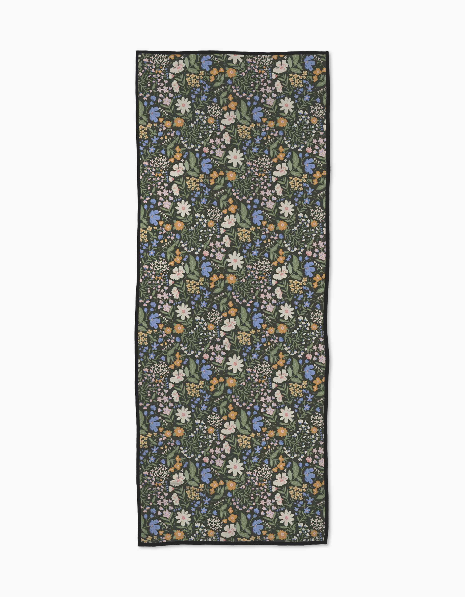 The Danelys Sidron Wildflower Vine Blush scarf showcases dense white, blue, and yellow floral patterns with green leaves on a dark background, inspired by recycled yoga towels and displayed flat on a white surface.