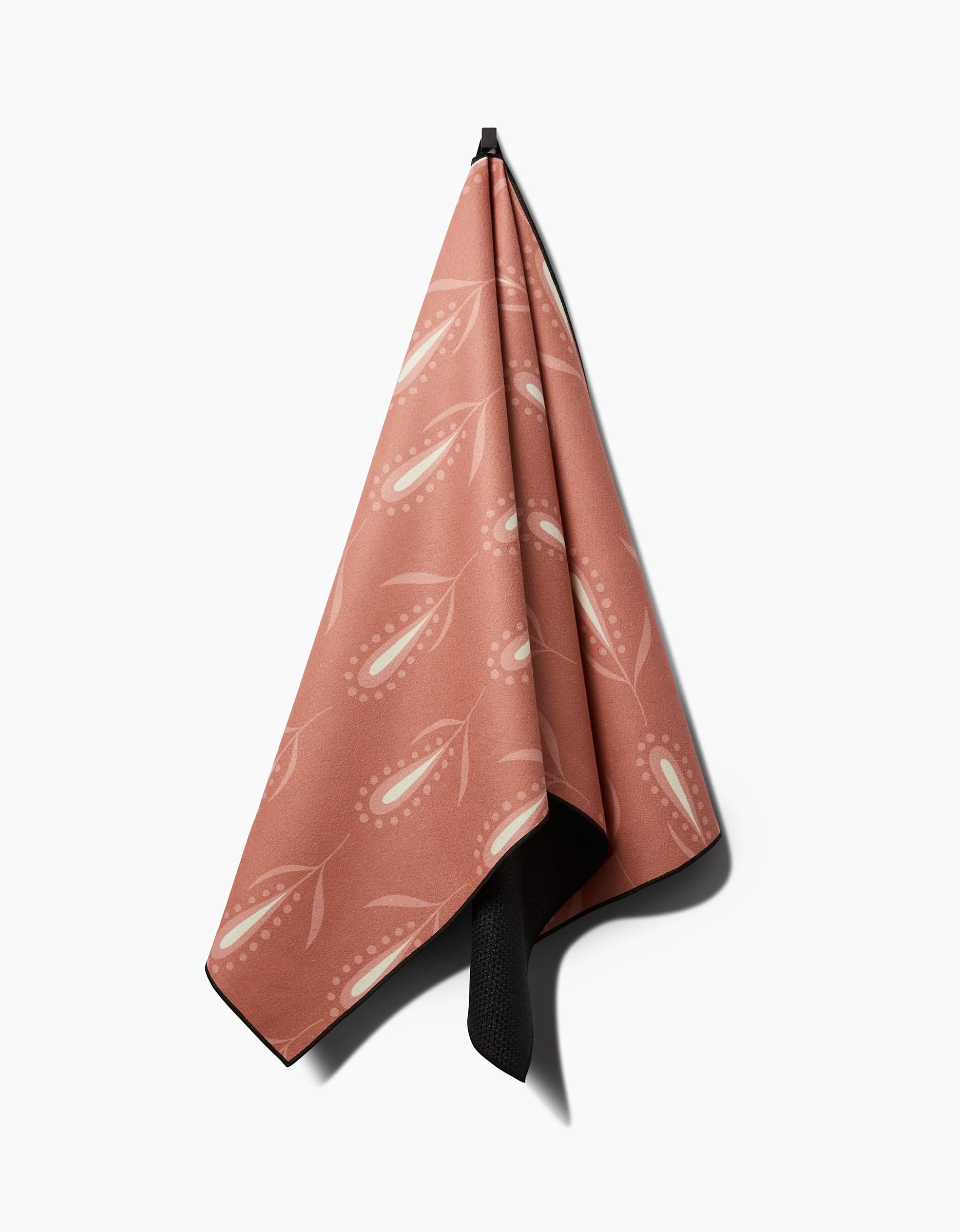 The Amita Nair Wilds yoga towel features a soft pink hue with a white abstract floral design, hung neatly against a white background—a perfect slip-resistant towel for your yoga practice.