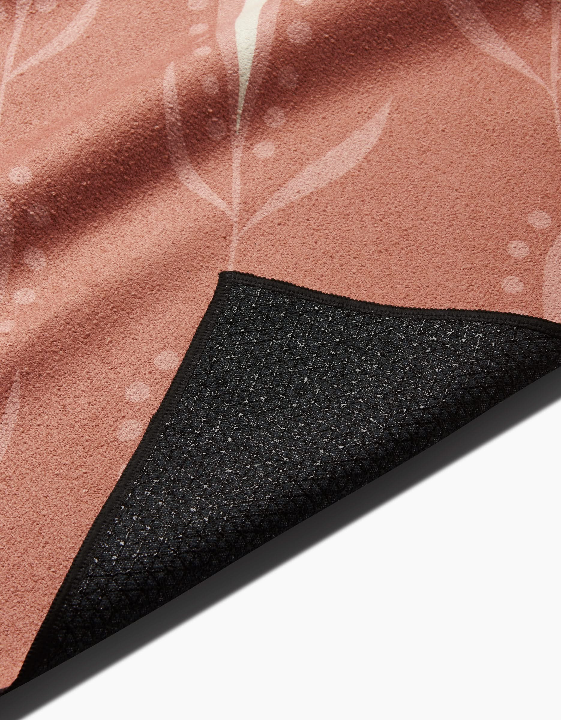 The Amita Nair Wilds pink yoga towel features a subtle leaf pattern and a black textured non-slip backing, with one corner folded to display both sides. This stylish, slip-resistant towel offers stability for your practice.