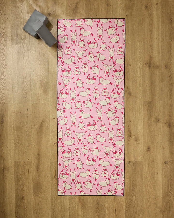 The Geometry Yoga Sheep mat features playful sheep poses on pink, resting on wood with a gray yoga block and recycled towel for extra comfort and eco-friendly support.