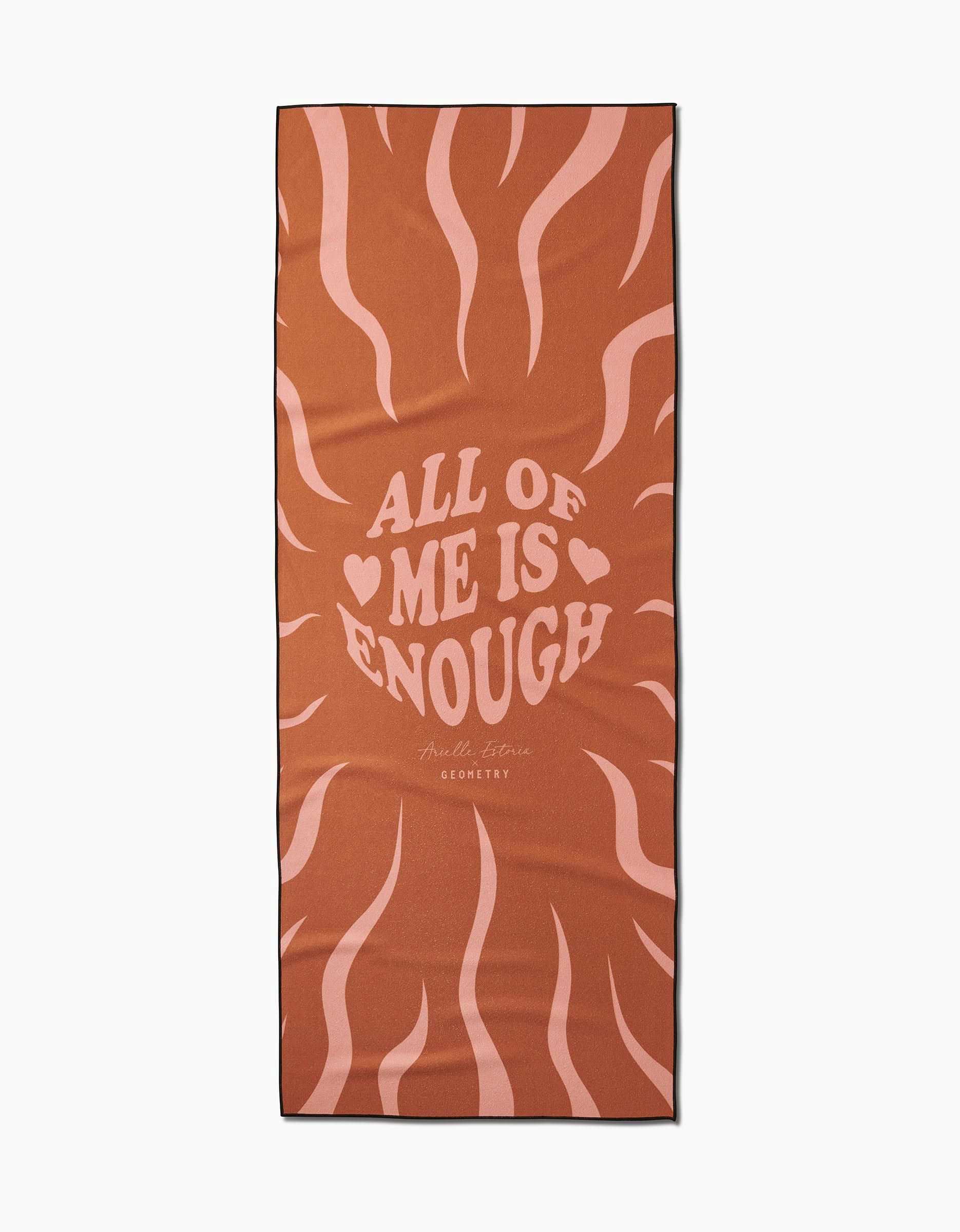 Arielle Estorias You are ENOUGH yoga towel is rectangular, made from recycled materials with a brown background and pink wavy lines. It features ALL OF ME IS ENOUGH, hearts, and Arielle Estoria’s signature for GEOMETRY.