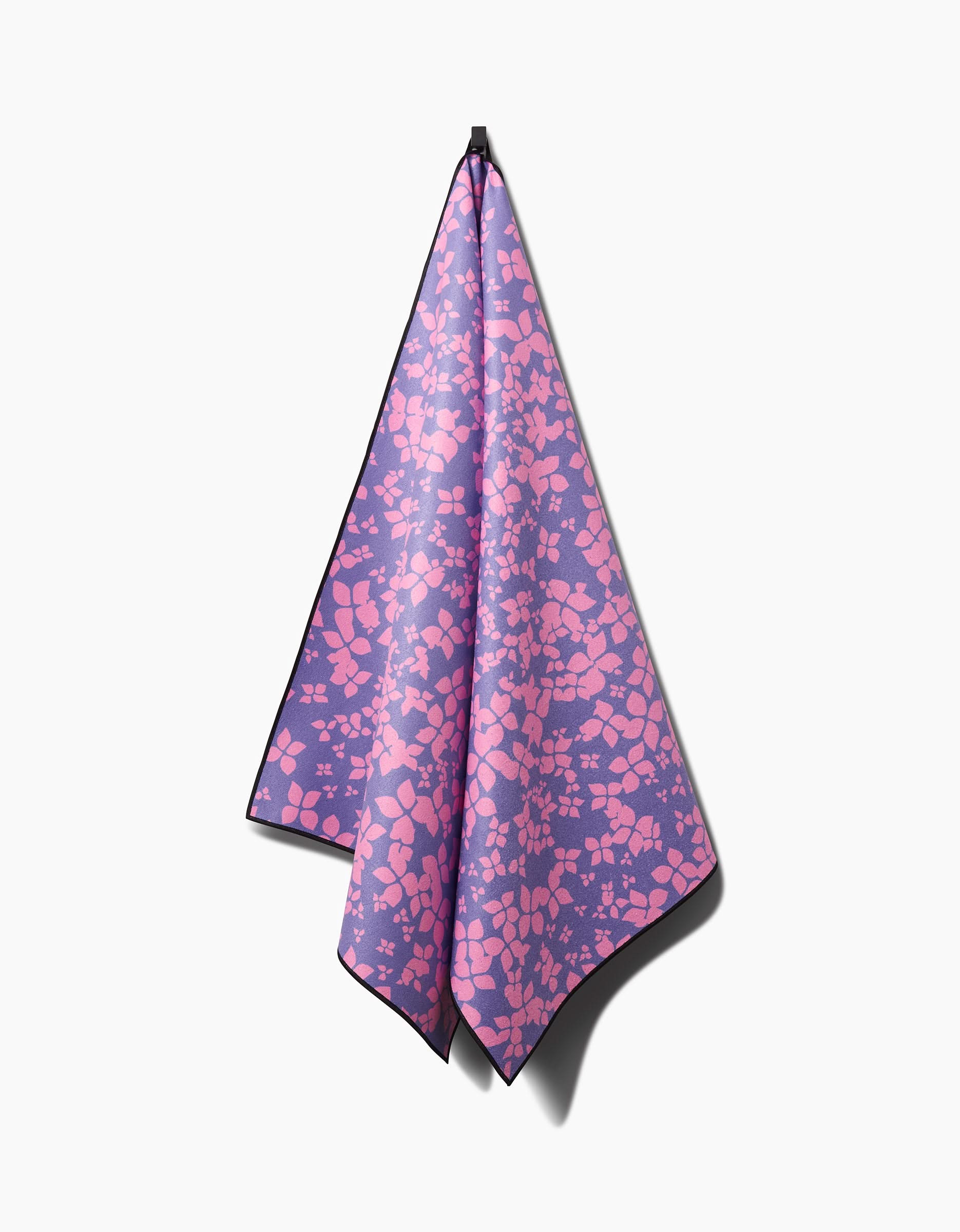 The Sareka Unique You Give Me Butterflies yoga towel, crafted from recycled materials and featuring pink abstract shapes on purple, hangs from a single hook against a white background with a soft shadow.