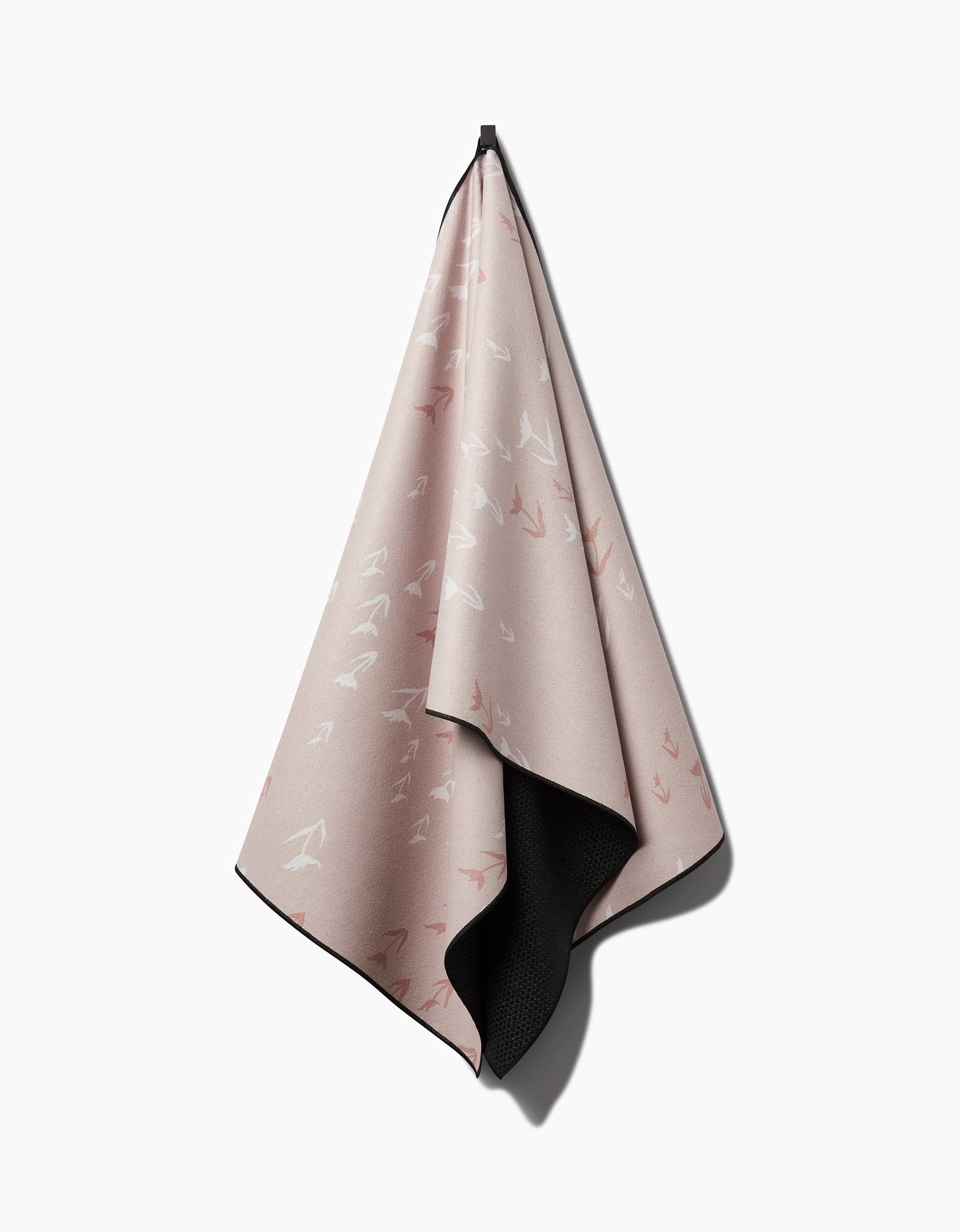 The You Grow Girl yoga towel by Aubrey Fairchild is light pink with white and red arrow patterns, a black underside, and a neat border. Made from recycled materials, its shown hanging from a hook on a plain white background.