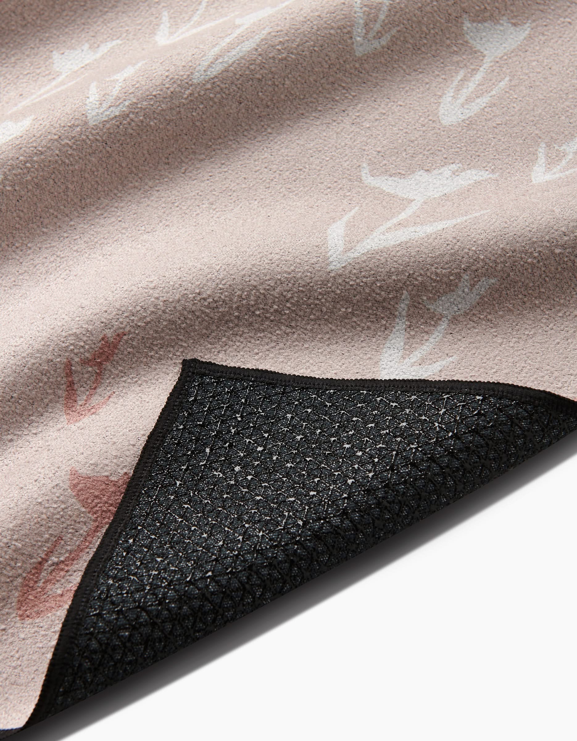 A close-up of the You Grow Girl yoga towel by Aubrey Fairchild in soft light beige with a subtle bird pattern, showing its textured black silicone non-slip grip backing on one corner.