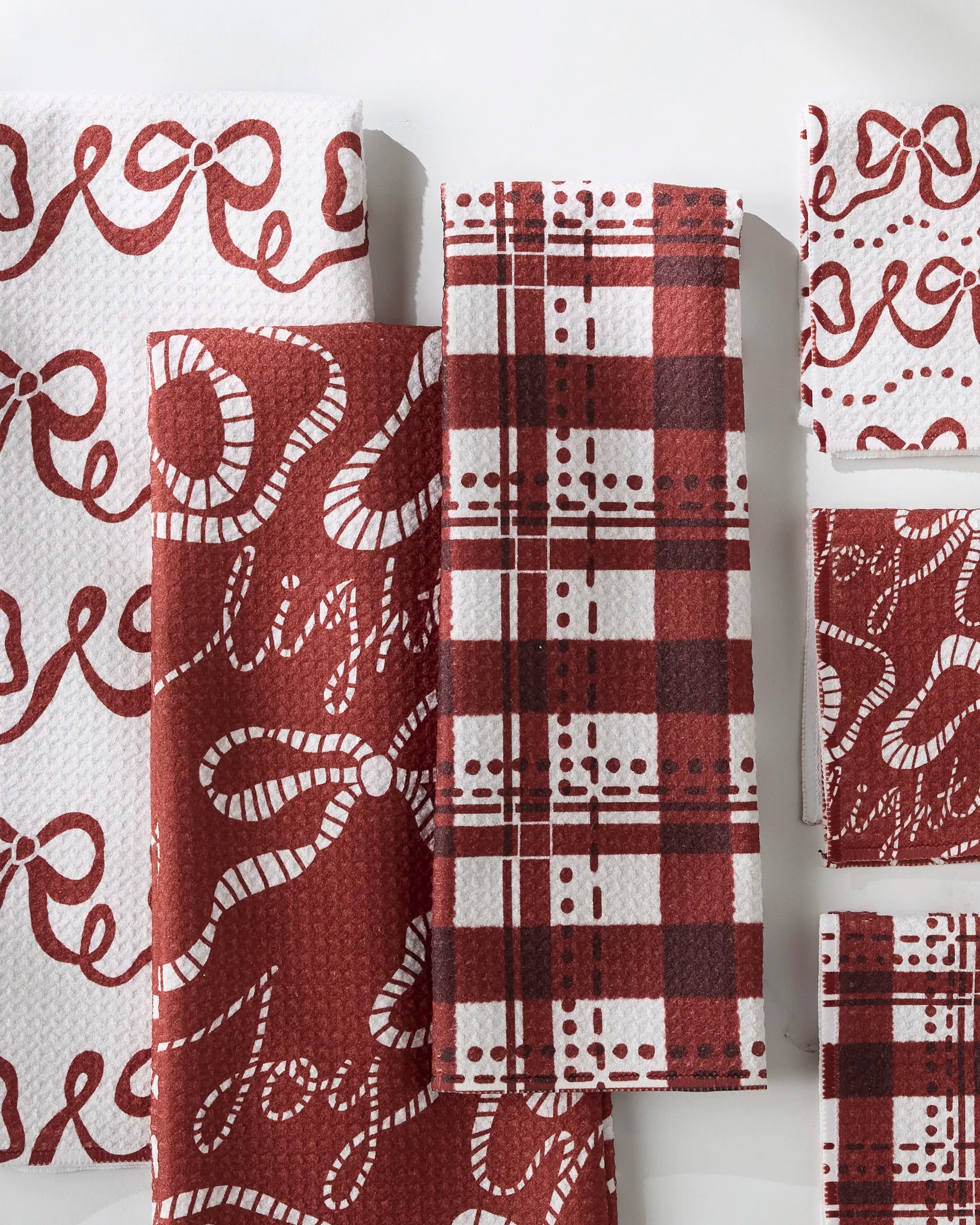 GEOMETRY’s “Cheerful Bows” napkins, featuring red and white holiday designs like plaid, candy canes, bows, and “joy,” are neatly arranged on a white surface.