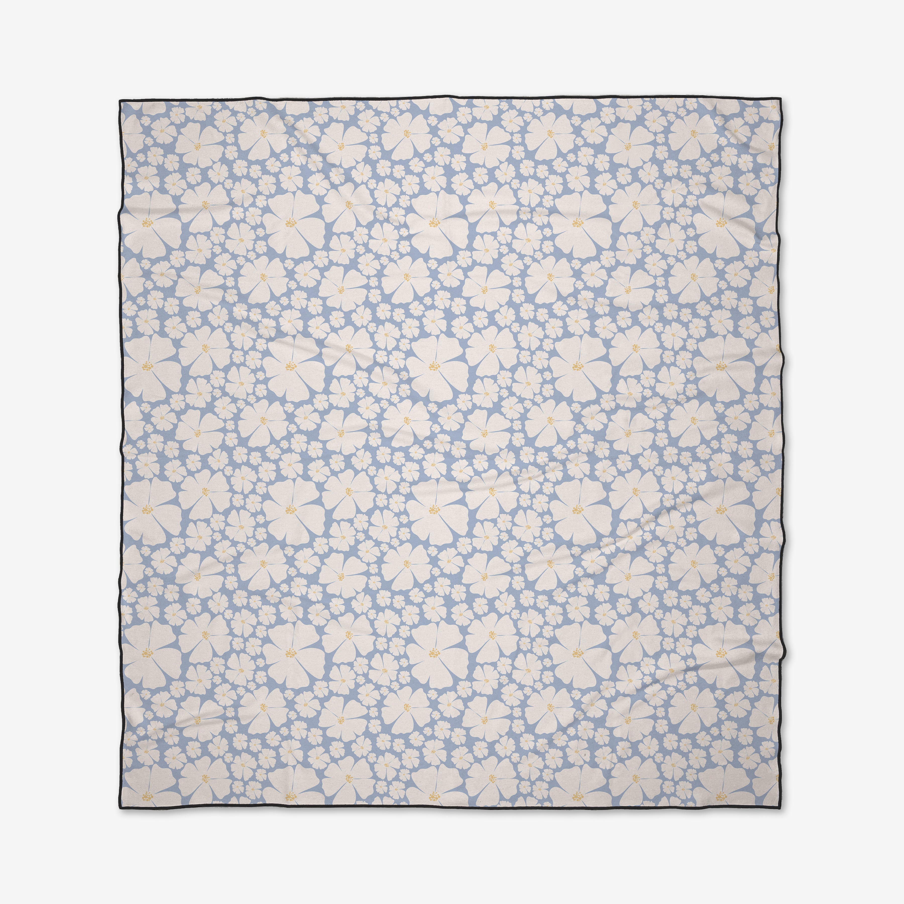 The Daisy Girl Blue beach blanket from Charlie Rowan Designs features a light blue background with white and light yellow hibiscus flowers with orange centers. Quick-drying and made from recycled materials, it’s finished with a thin dark border.