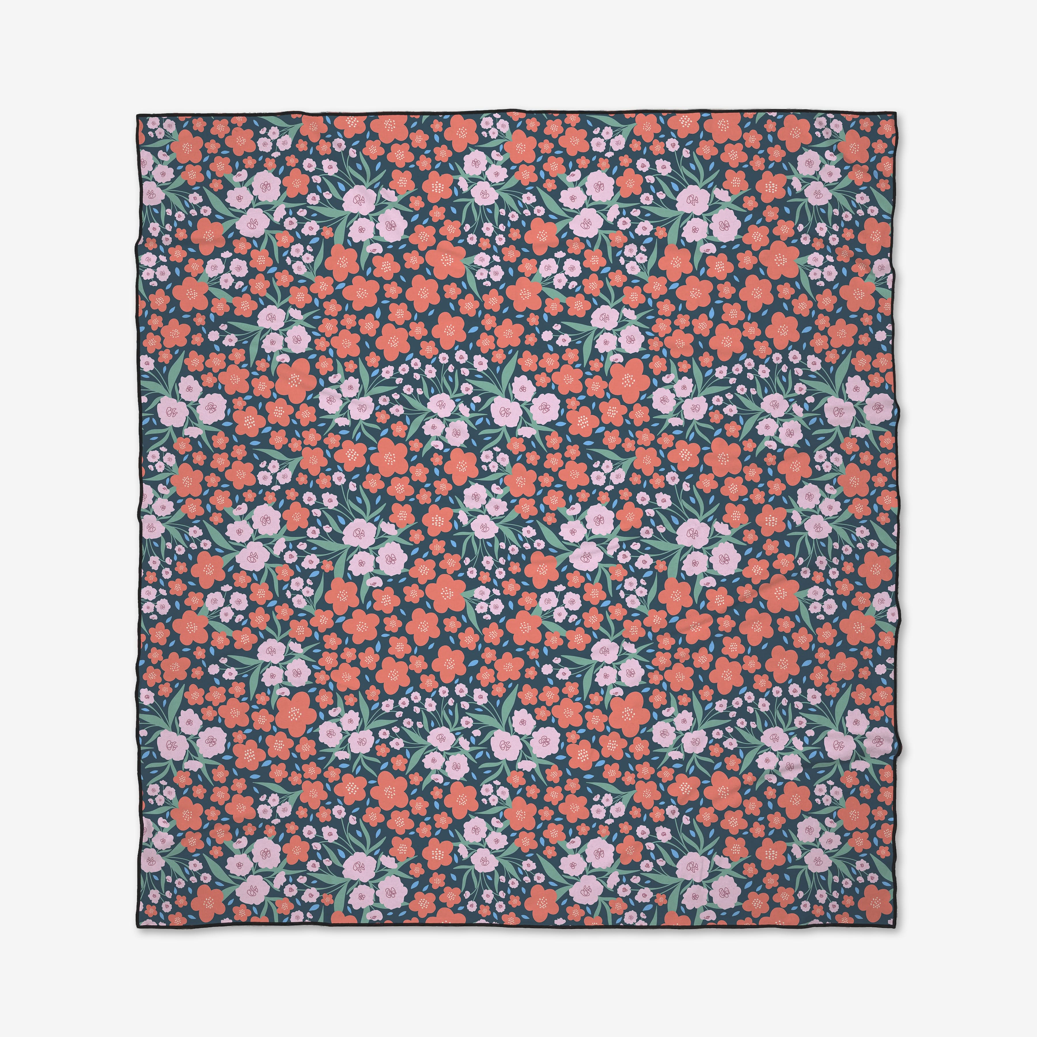 The Daydreamer beach blanket by Charlie Rowan Designs features a dense floral pattern with pink and coral flowers and green leaves on a dark background, creating a vibrant look from closely arranged blooms. Made from recycled materials.