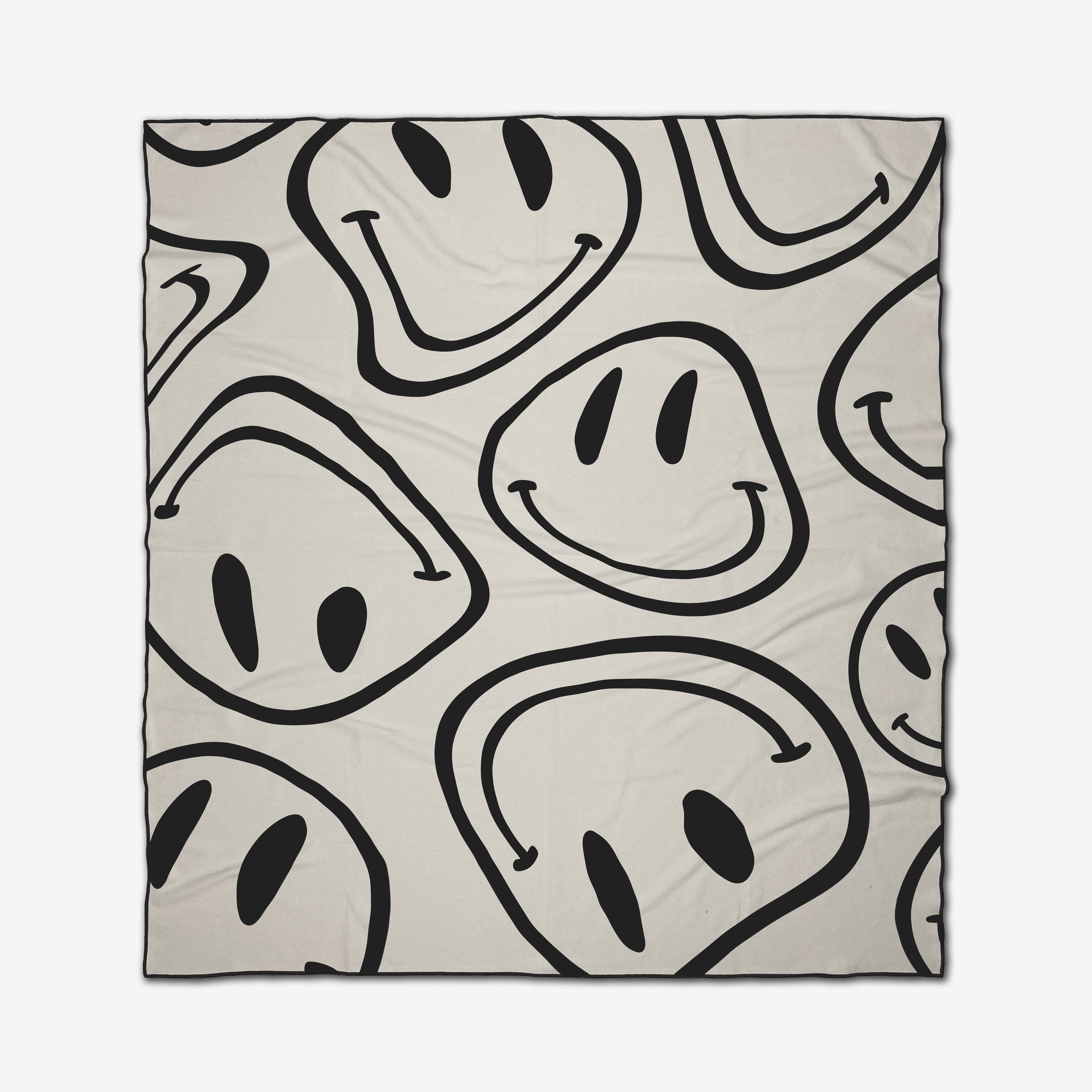 The GEOMETRY Mood Swing Light is a beige beach blanket with large, black, hand-drawn smiley faces facing various directions. Crafted from quick-drying recycled materials, it offers eco-friendly comfort for your beach days.