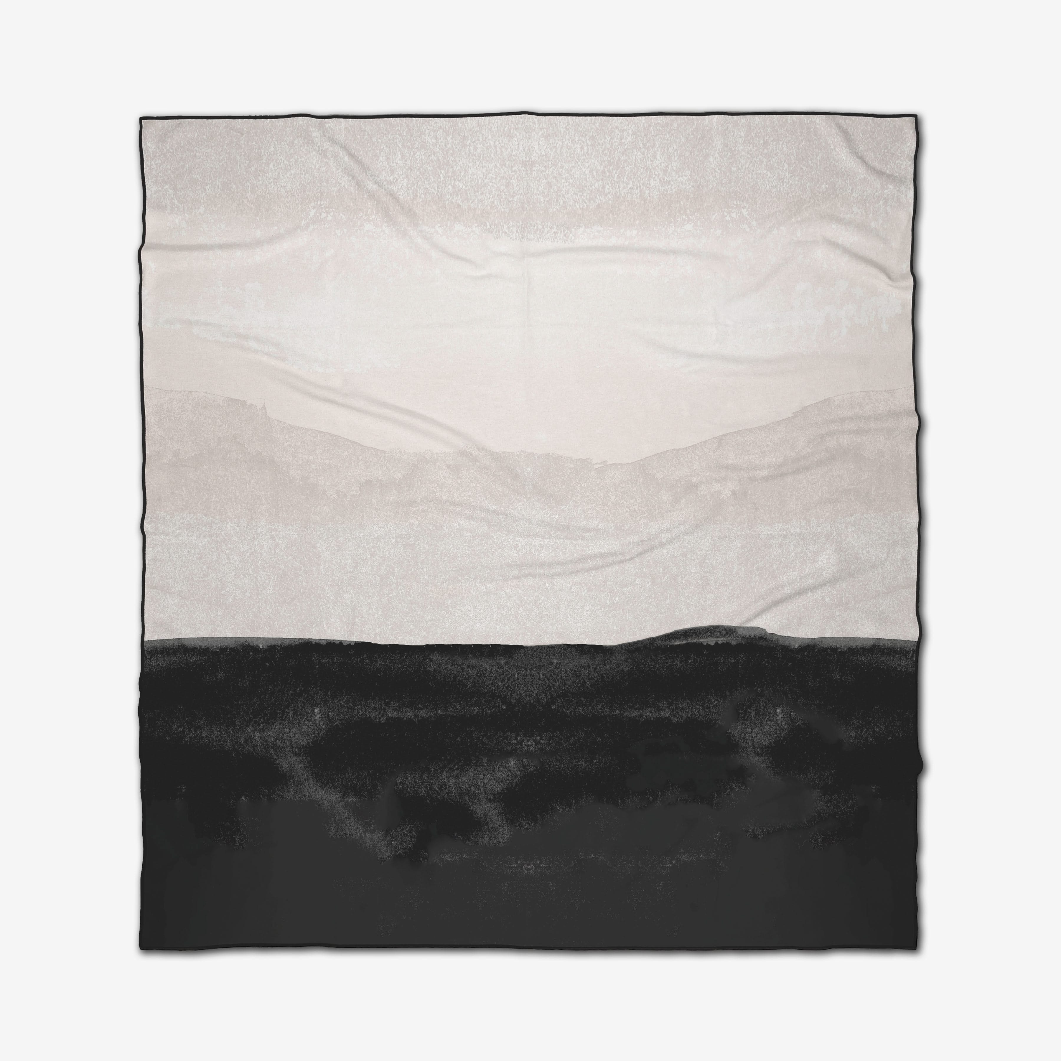 The GEOMETRY Top Layer is a square recycled beach blanket with a minimalist landscape design, featuring a black land-like foreground and light gray and white mountains and sky. Visible fabric creases add an organic touch.