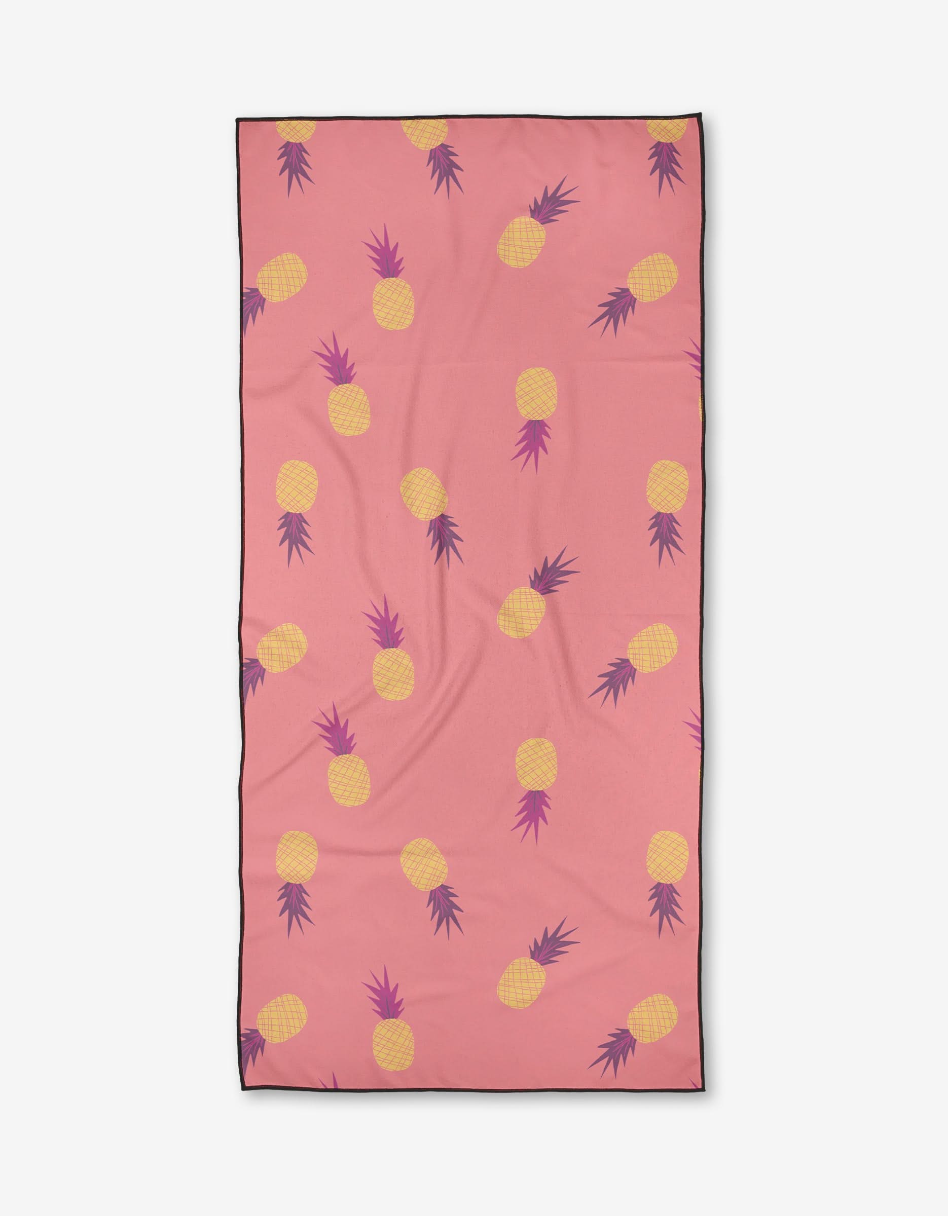 The Ananas by Jessica Swift is a compact beach towel featuring a pink background with repeating yellow pineapples, purple leaves, and a black border. Made from quick-drying fabric for easy use.