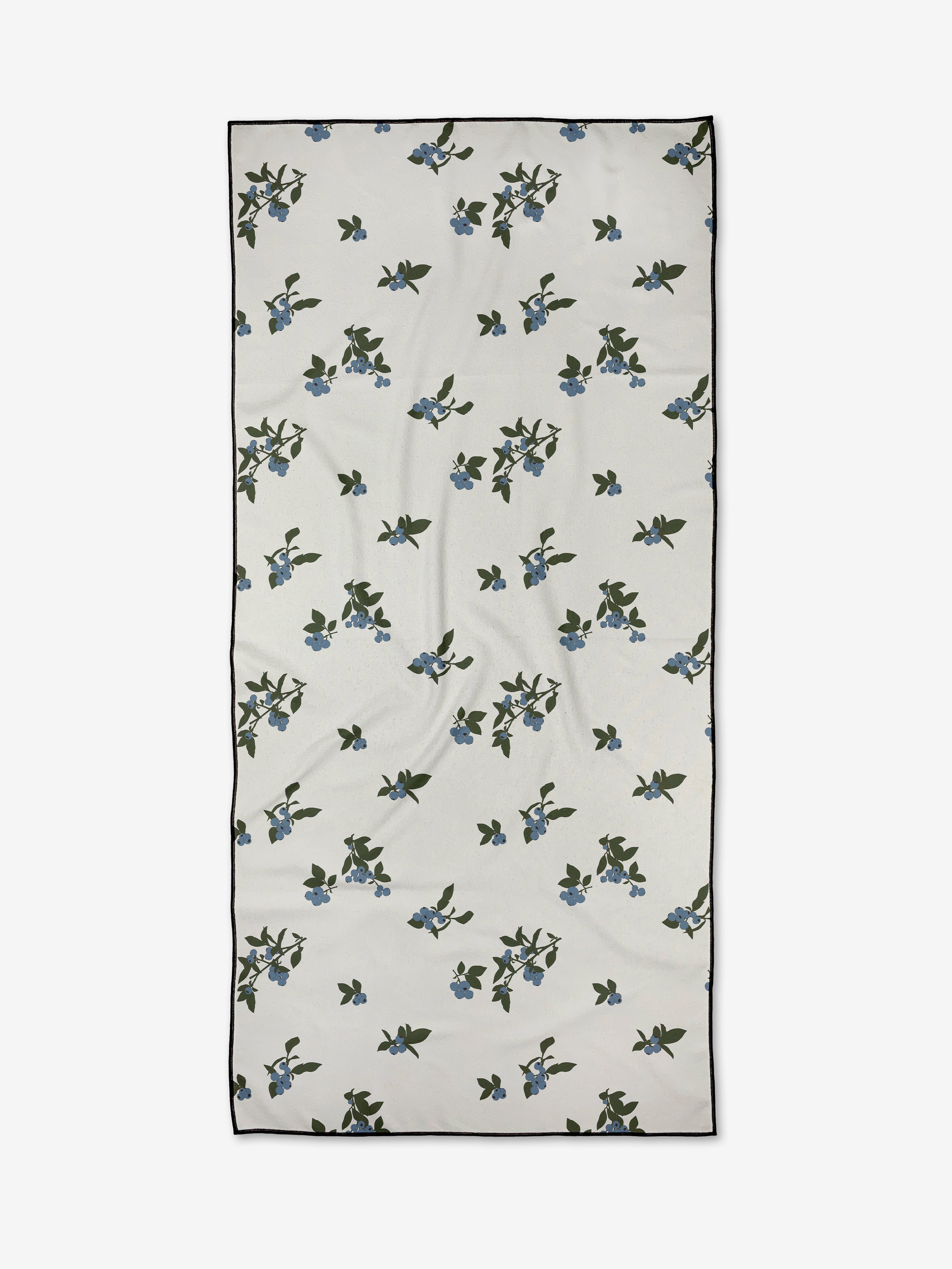 Aubrey Fairchild’s Blueberries is a rectangular white compact beach towel, adorned with scattered green leaves and small blue flowers, finished with a thin black border.