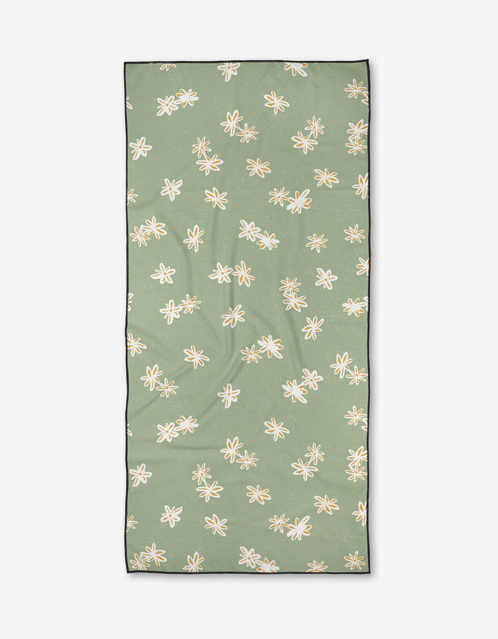 The Ashley Celena Citrus Blossoms beach towel is rectangular, green, made from recycled materials, and features a repeating white and yellow floral pattern with a thin black border, shown laid flat on a white background.