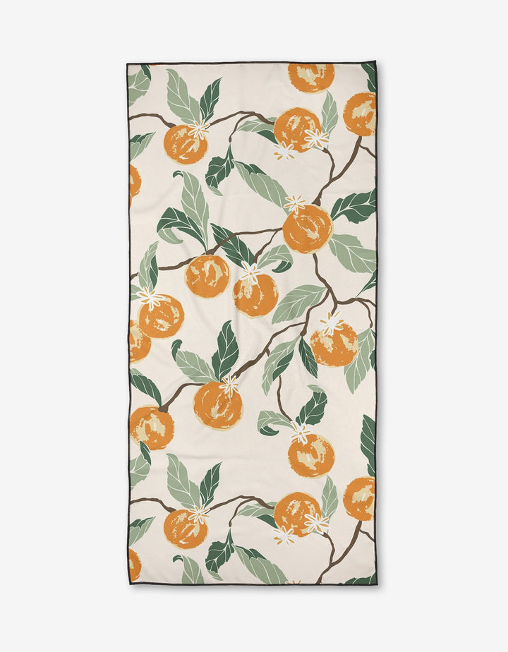 The Citrus Dreams beach towel by Ashley Celena features orange apricots, green leaves, and white flowers on branches against a cream background with a black border. Made from quick-drying recycled materials.