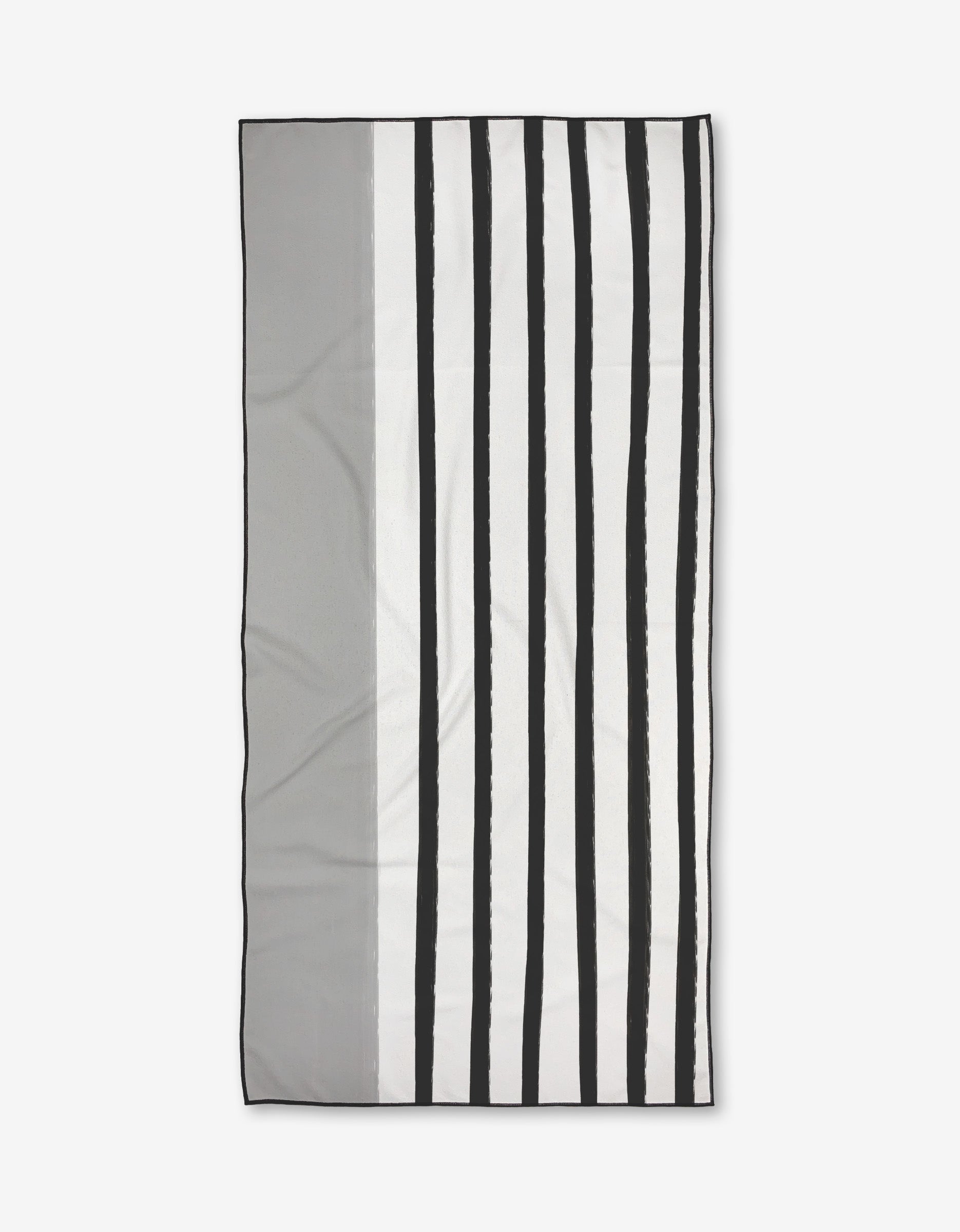 The Dawn beach towel by Kailee Wright is rectangular with a minimalist design—vertical black and white stripes on the right, solid gray on the left. Made from quick-drying recycled materials, its pictured against a plain white background.