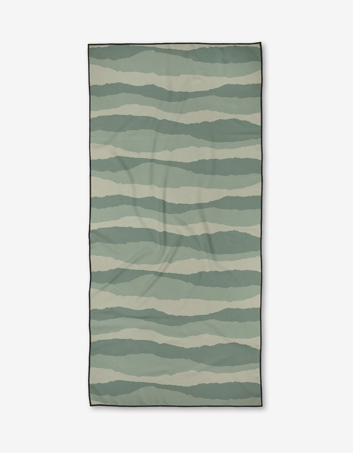The Twig + Spark Distant Landscape Micro-loop Beach Towel features horizontal wavy stripes in green and beige, a thin black border, and is made from quick-drying, post-consumer recycled materials.
