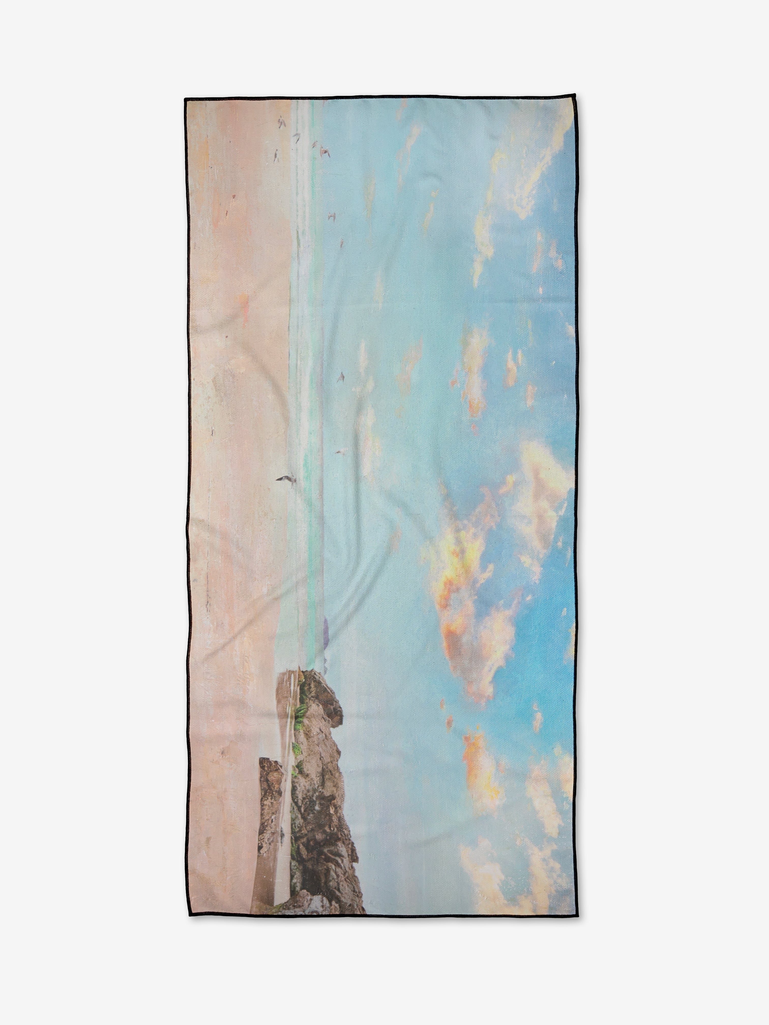 The Empyreum beach towel by Stefanie Bales features a printed sunny beach scene with blue sky, clouds, and rocky foreground. Rectangular and crafted from quick-drying, recycled materials for sustainable convenience.