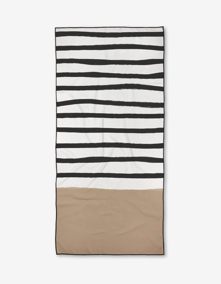 The Kails beach towel by Kailee Wright features uneven black stripes on white at the top and a solid beige bottom. Made from recycled materials, it is quick-drying and convenient for your beach days.