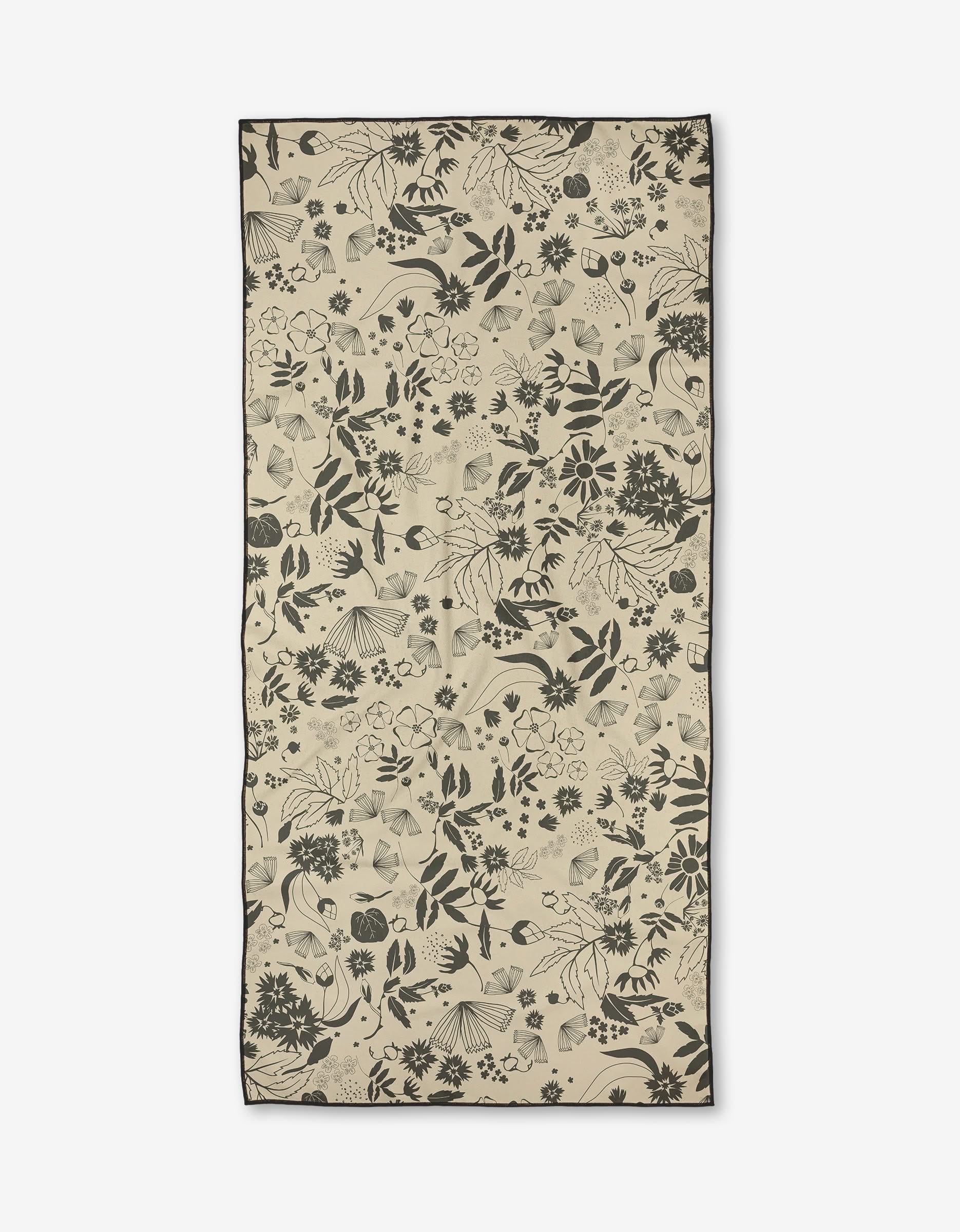 The Scattered Floral by Ash Cascade is a rectangular beige micro-loop beach towel with an intricate black botanical and floral pattern, made from quick-drying recycled materials.