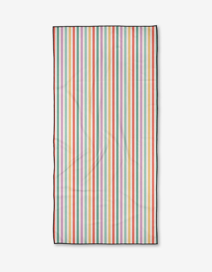 The Summer Stripes beach towel by Charlie Rowan Designs is compact and made from recycled materials, featuring vertical stripes in pink, orange, yellow, green, blue, and white with a thin black border on a white background.
