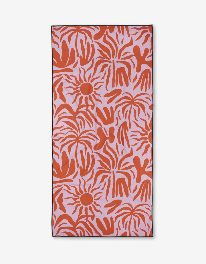 The Summer Sunset beach towel by Marina Solodka features a pink background with bold, abstract red sun shapes and handprints. Made from quick-drying recycled materials, it has a black border and is shown on a white surface.