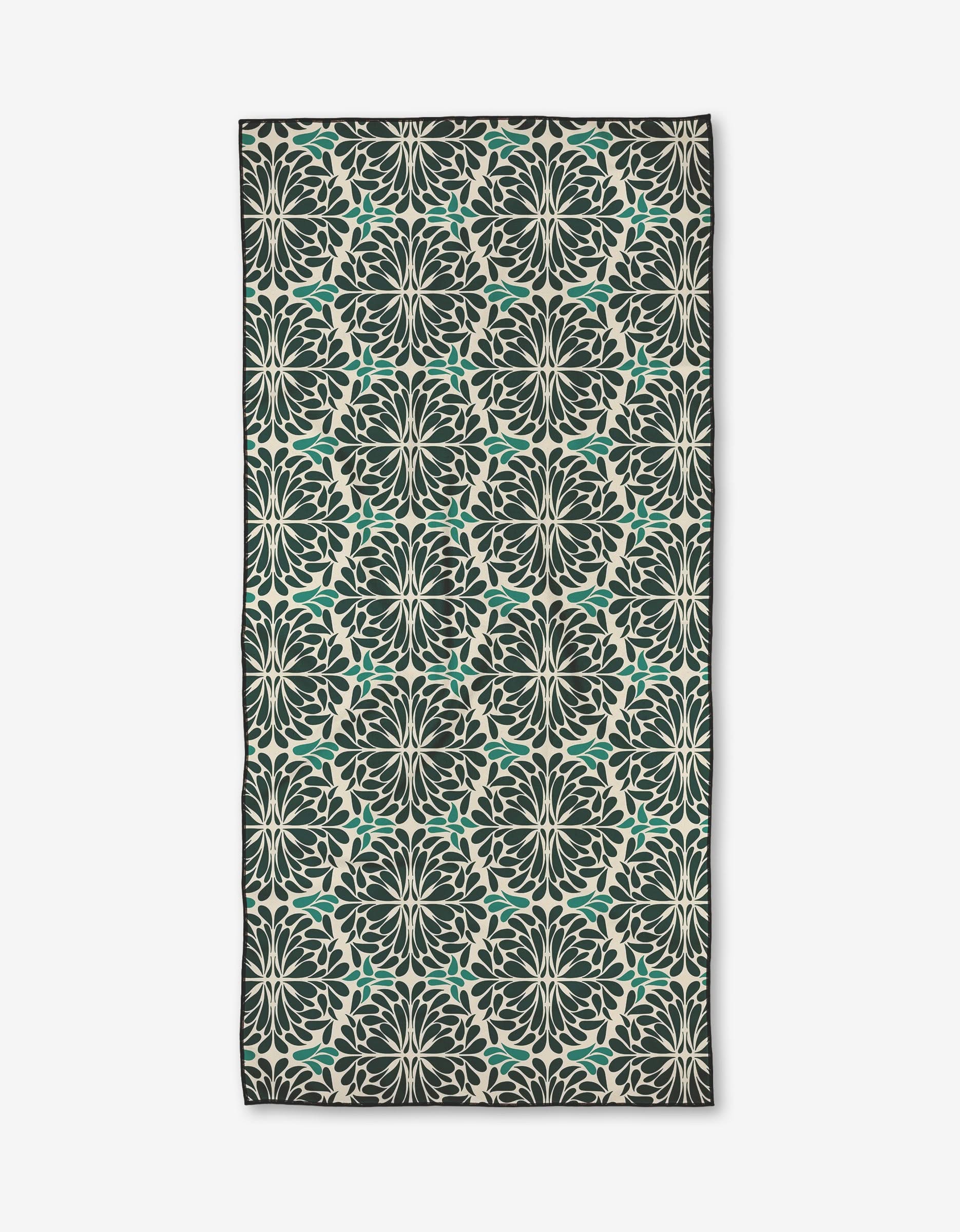 The Teal Pinwheel by Rebecca Woolbright is a rectangular micro-loop beach towel with a symmetrical floral pattern in dark green, teal, and cream, covering the entire fabric and bordered by a slim dark edge.